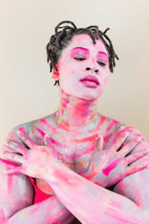 A person with dreadlocks and skin painted in vibrant pink and purple glittery streaks