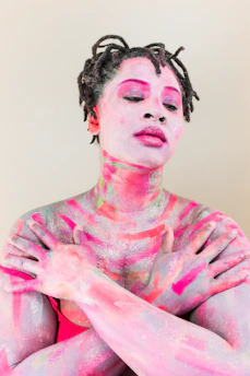 A person with dreadlocks and skin painted in vibrant pink and purple glittery streaks