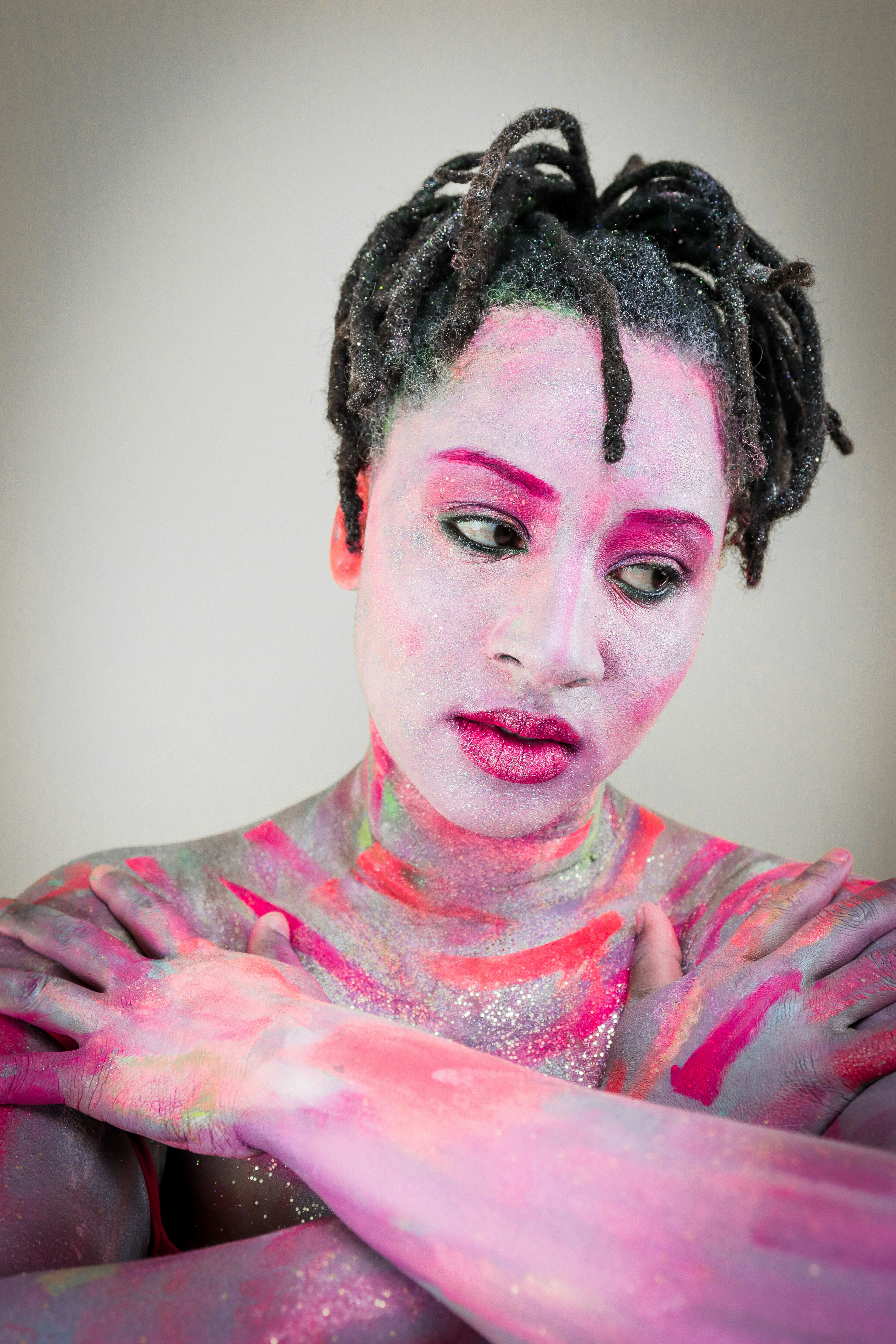 A person with dreadlocks and face and body painted in vibrant pink and purple