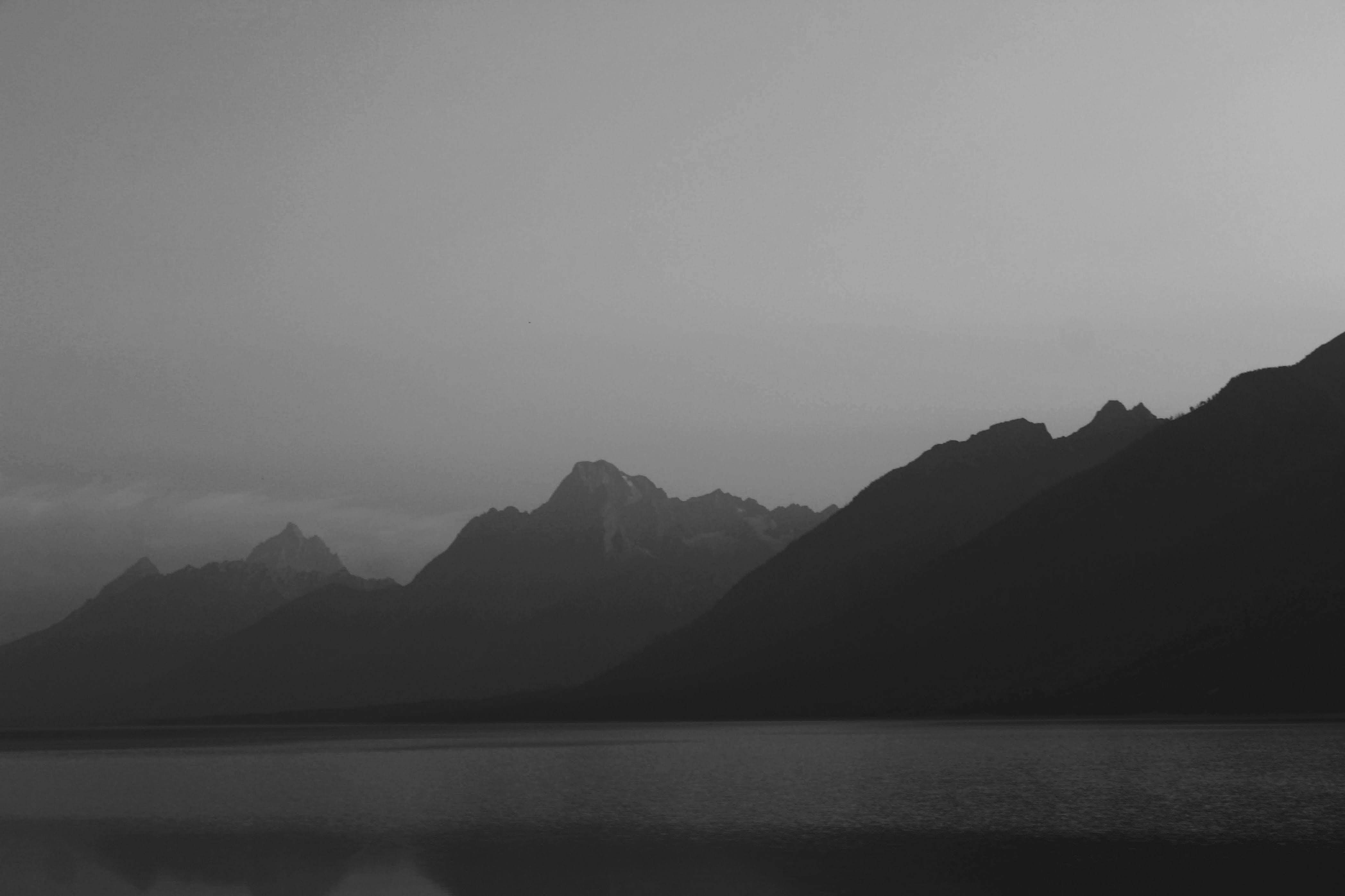 The Teton Range in silhouette above a calm lake in black and white