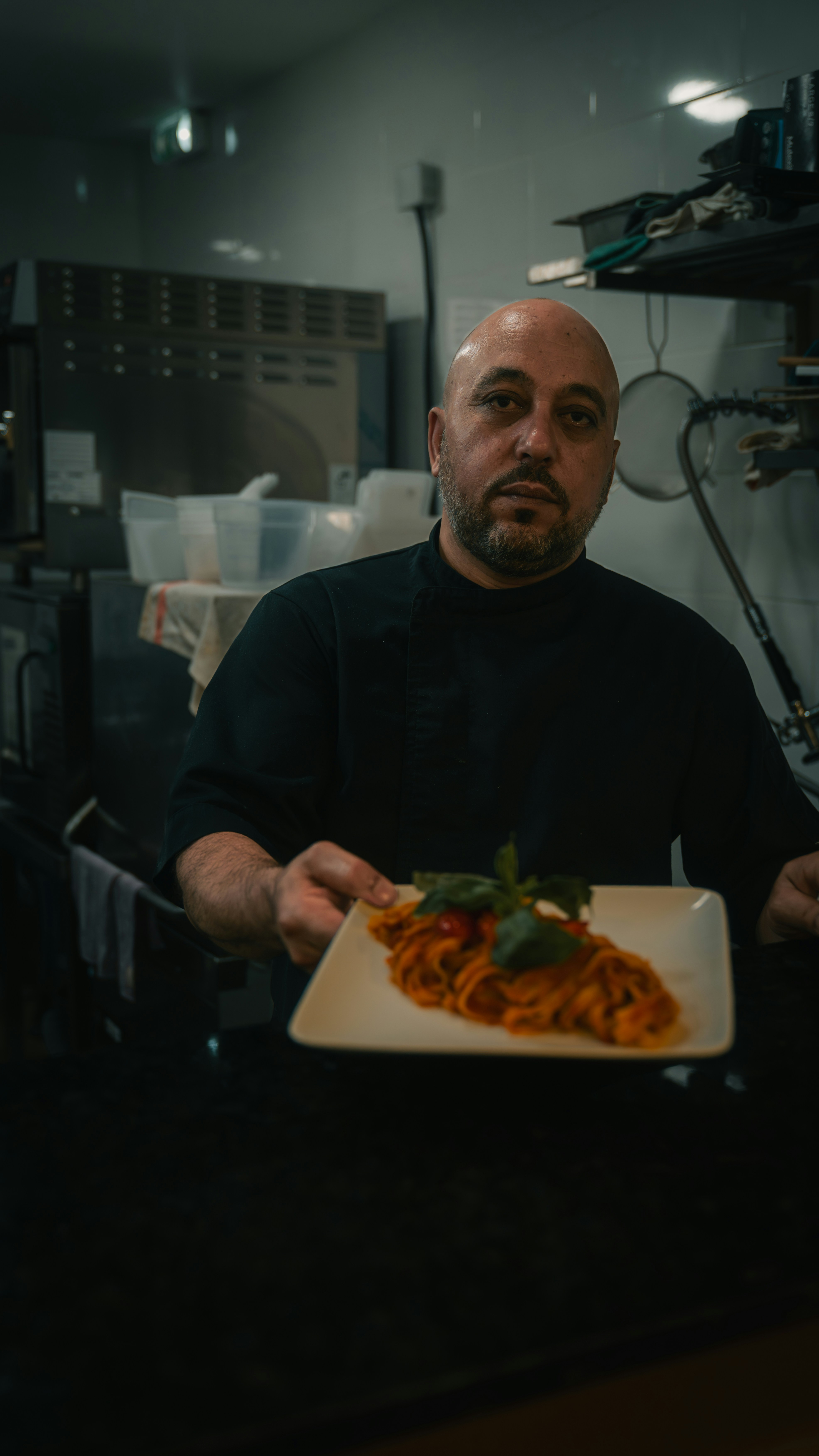A chef in a black uniform holding a plate of pasta in a kitchen