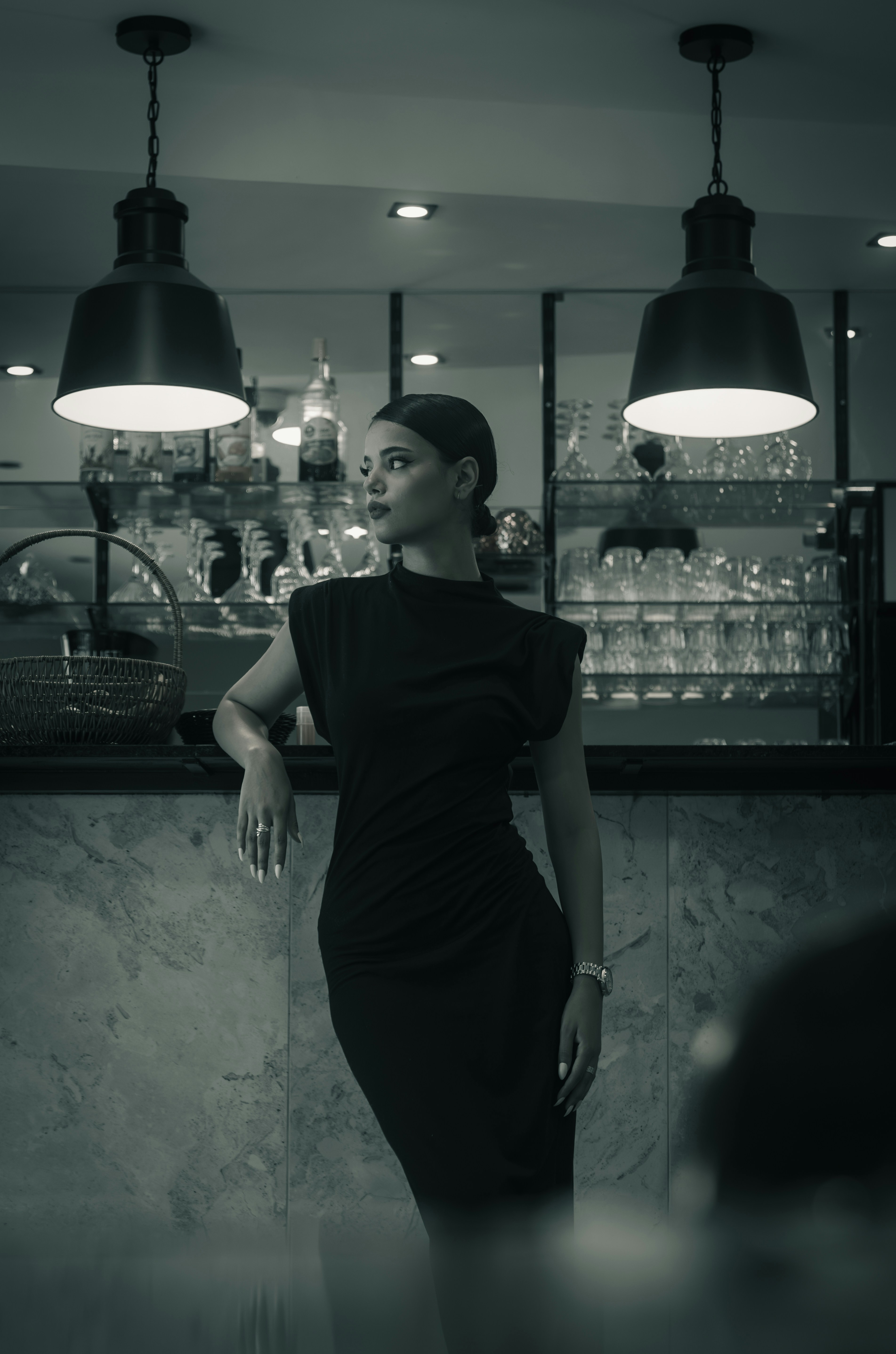 A woman in a black dress leaning against a marble bar in a lounge