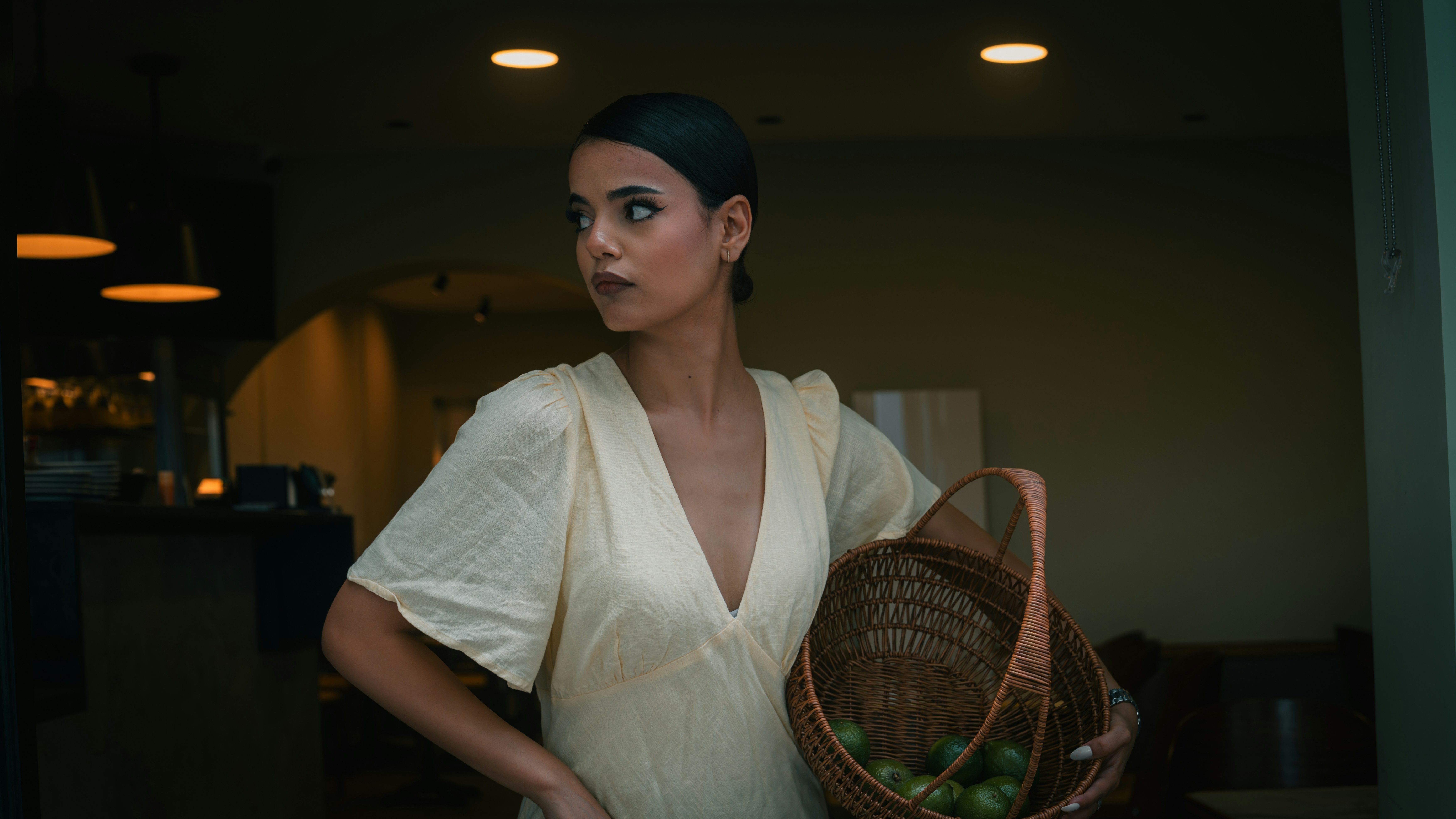 A woman in a pale yellow dress holding a wicker basket of limes