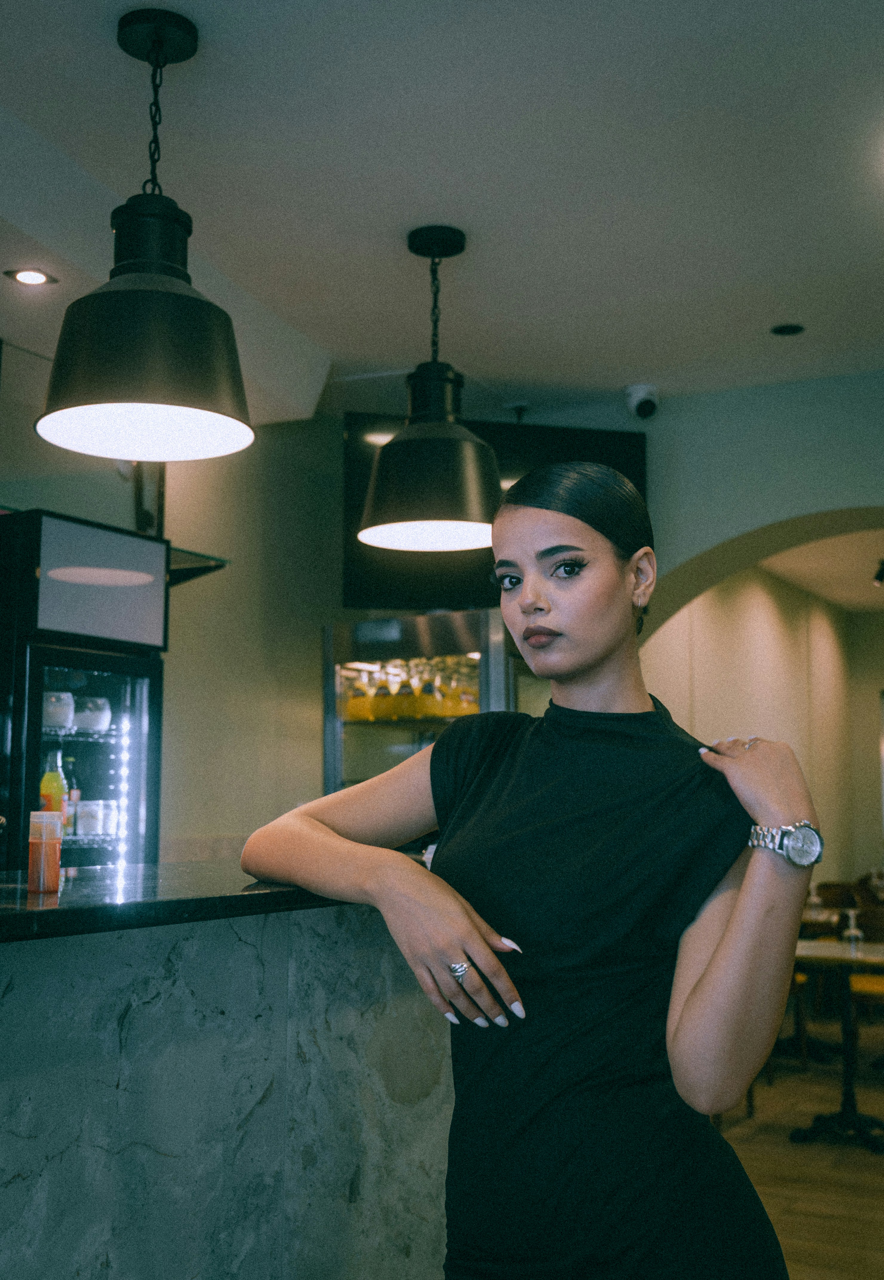 A woman in a black dress leaning against a marble bar in a cafe