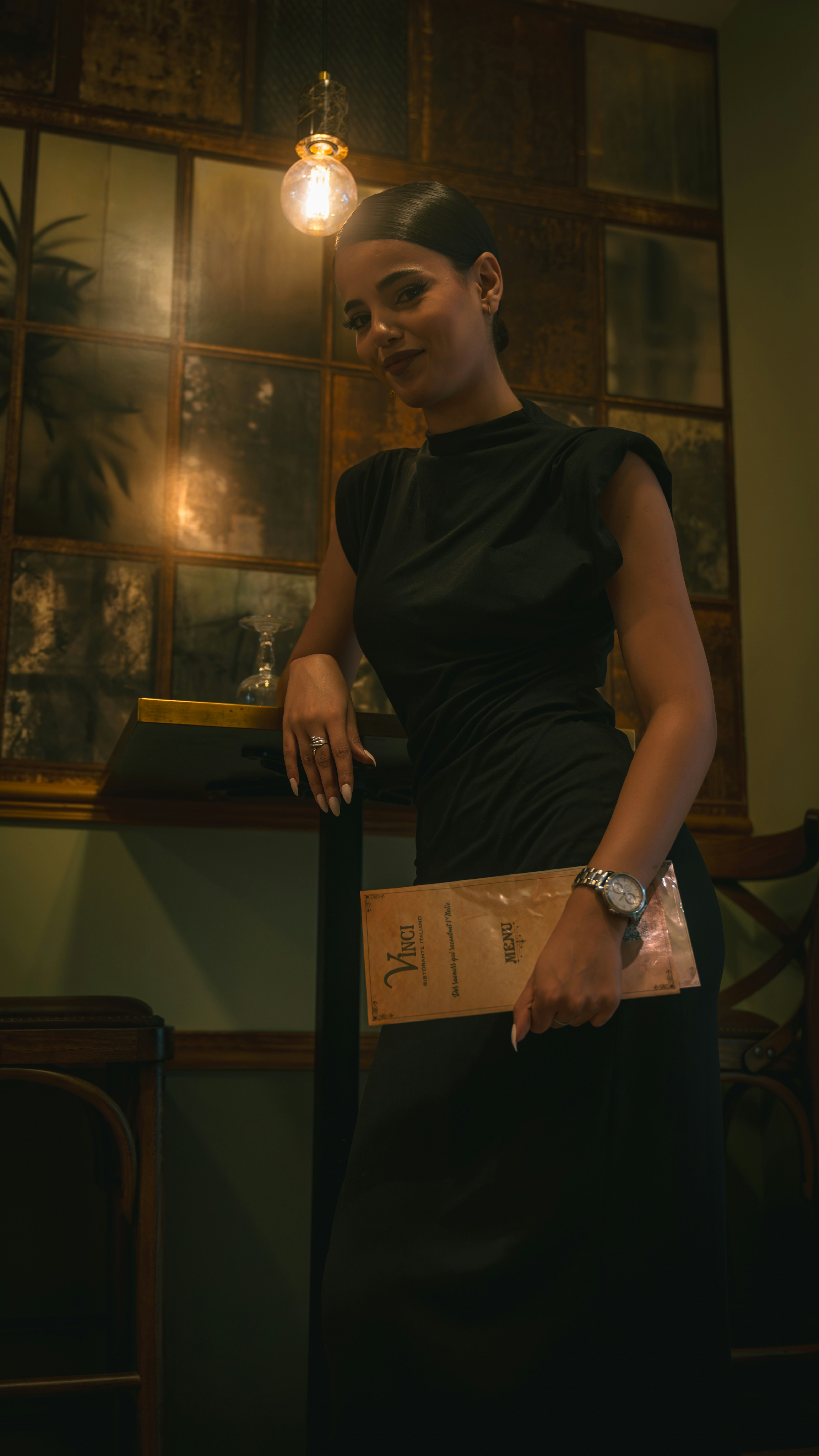 A woman in a black dress holding a menu in a dimly lit restaurant