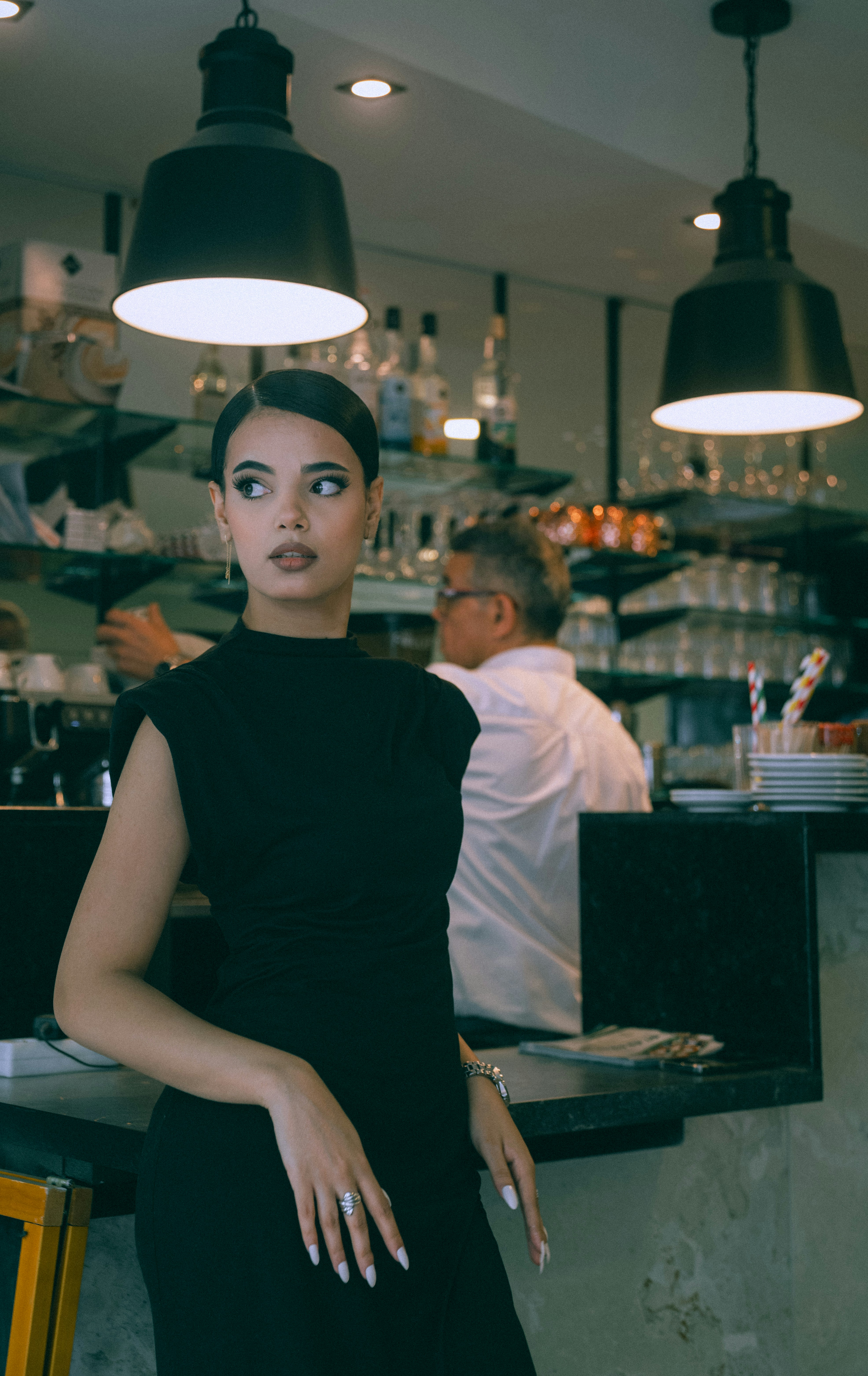 A woman in a black dress standing at a bar counter in a cafe