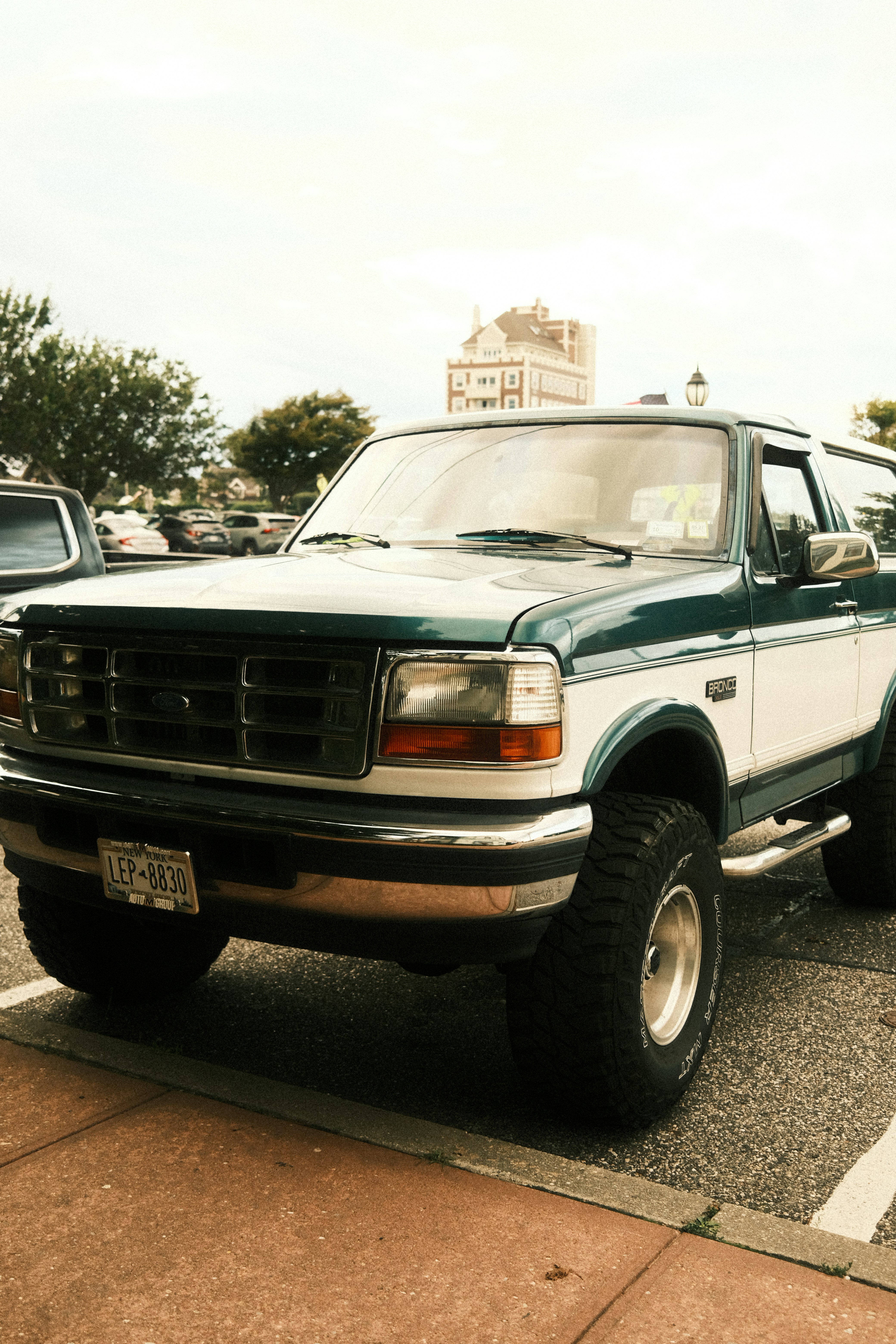 Um Ford Bronco bicolor, verde e branco, estacionado em um estacionamento asfaltado