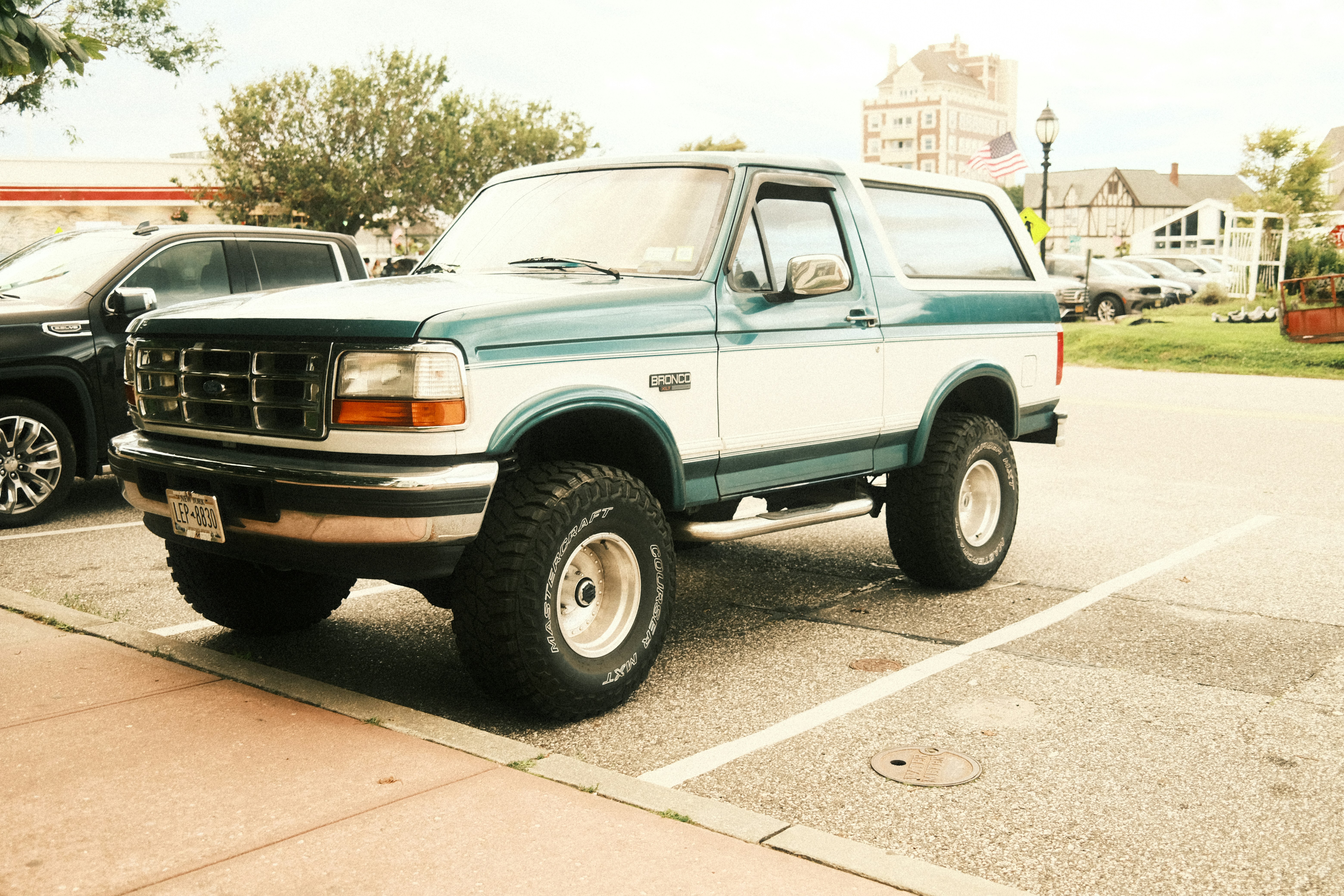 Um Ford Bronco bicolor, azul-petróleo e branco, estacionado em um estacionamento pavimentado