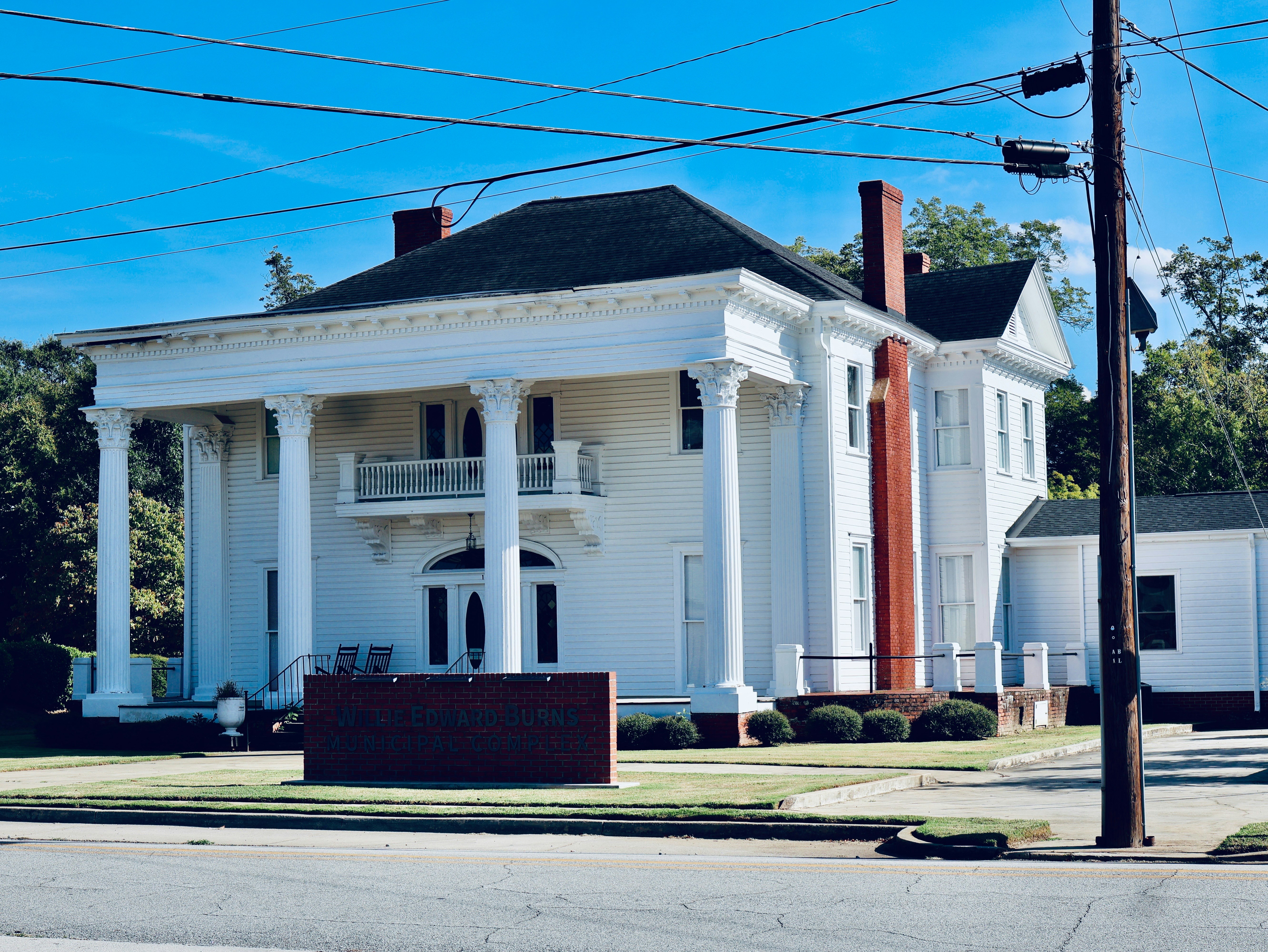 A white two-story building with tall columns and a brick sign in front