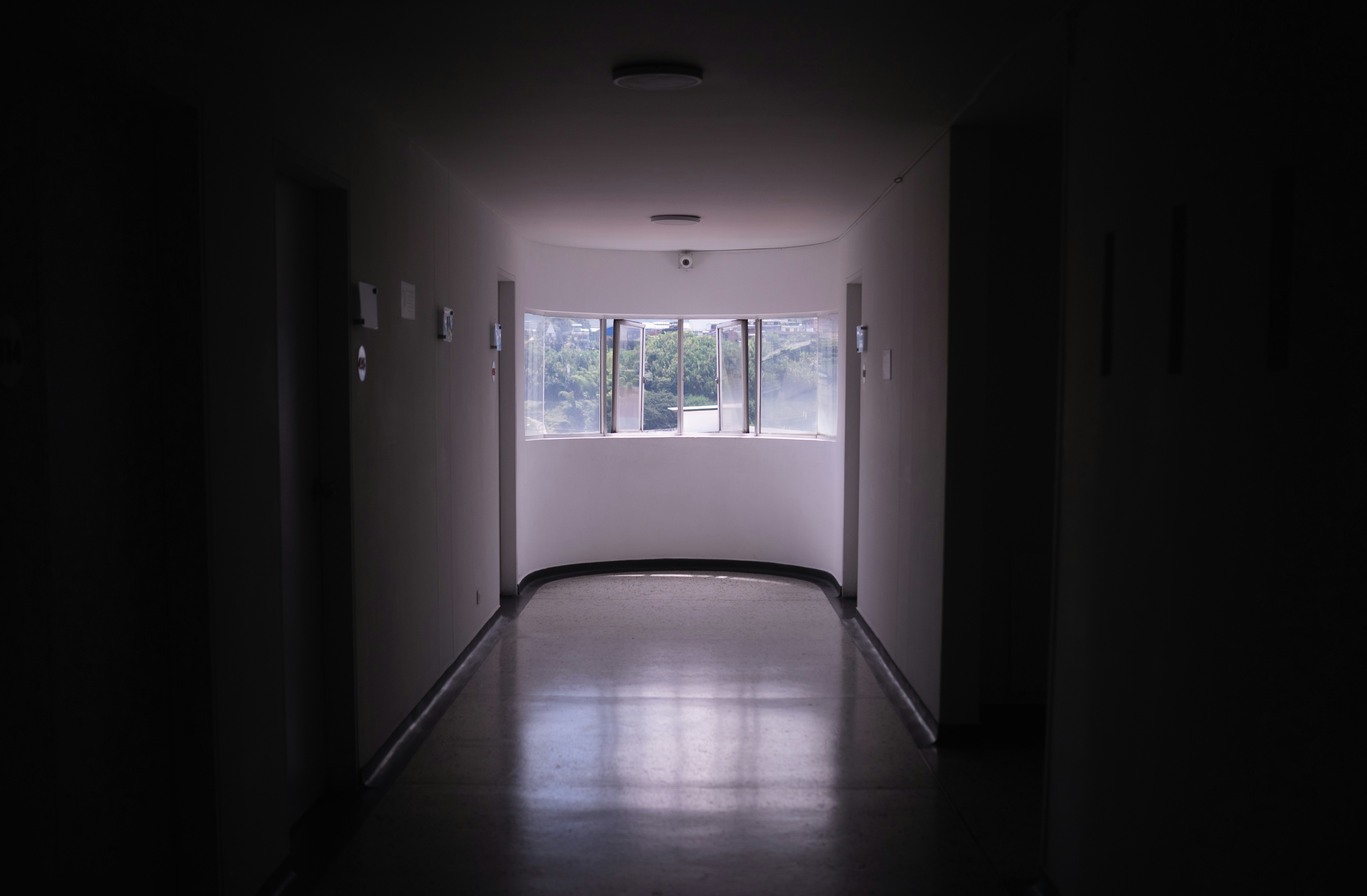 A dim hallway leading to a curved window overlooking green trees