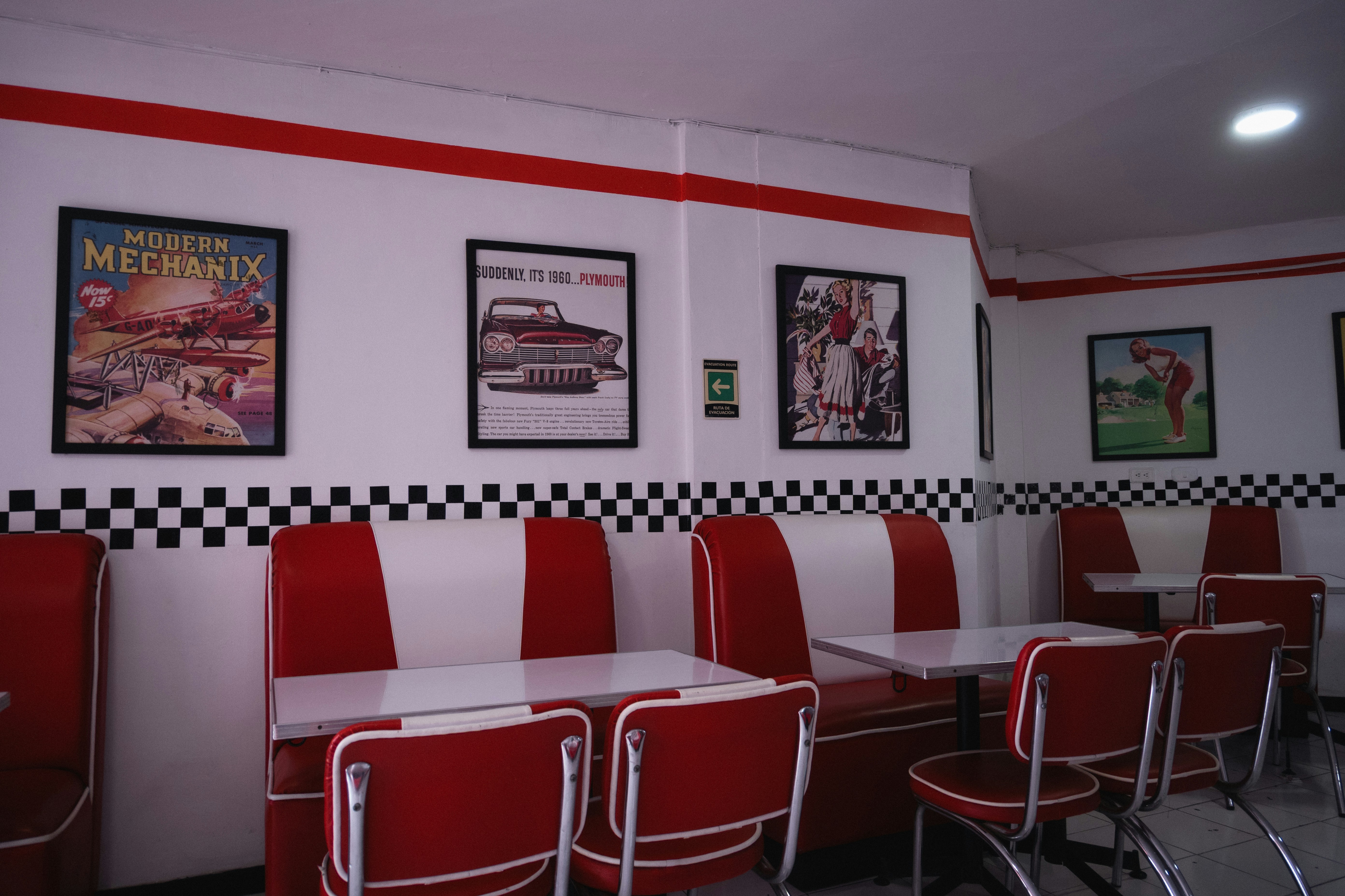 Retro diner interior with red and white booths, chrome chairs, checkered wall trim and vintage framed posters