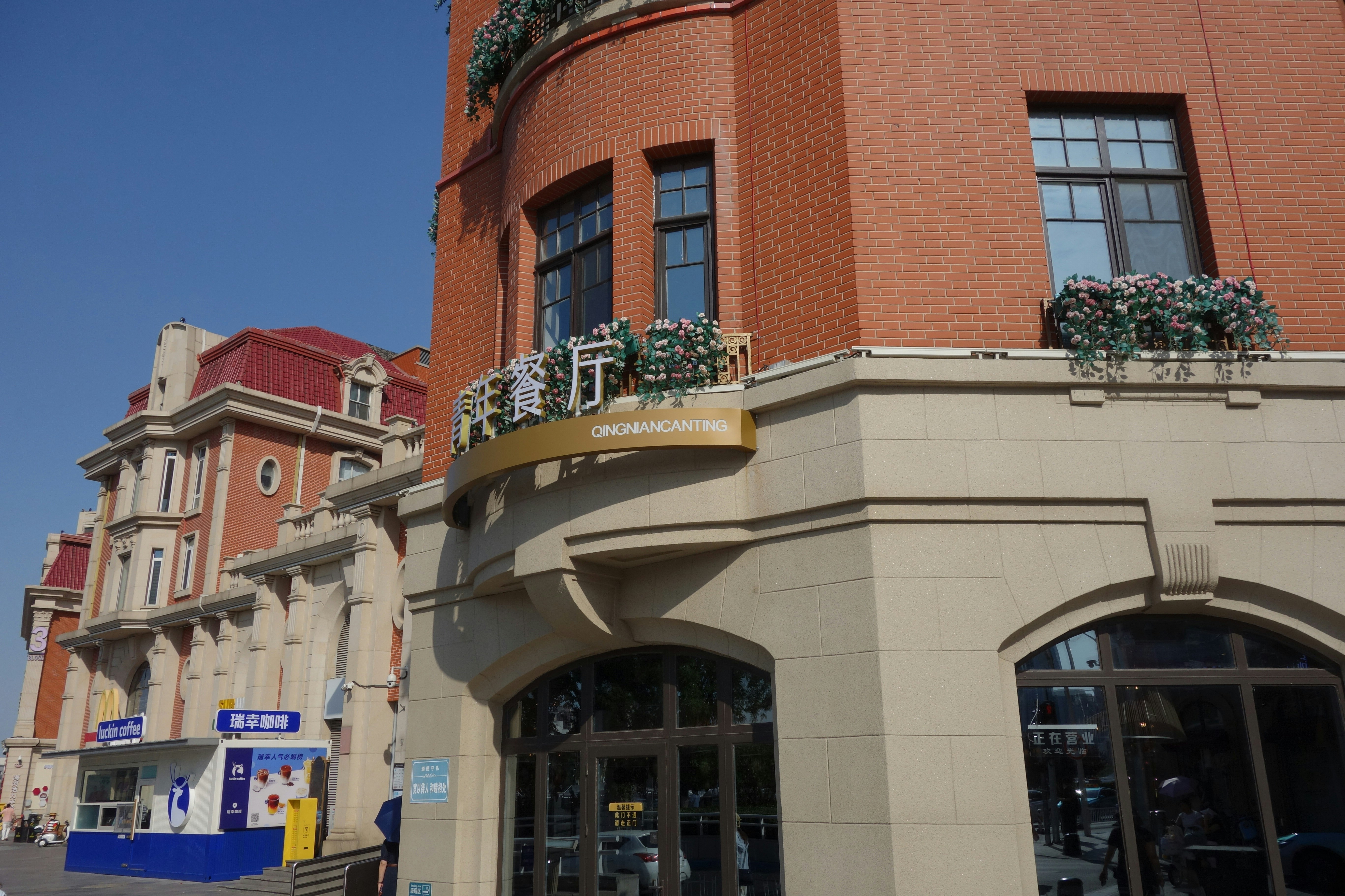 A red brick building with a sign reading QINGNIANCANTING above a stone storefront
