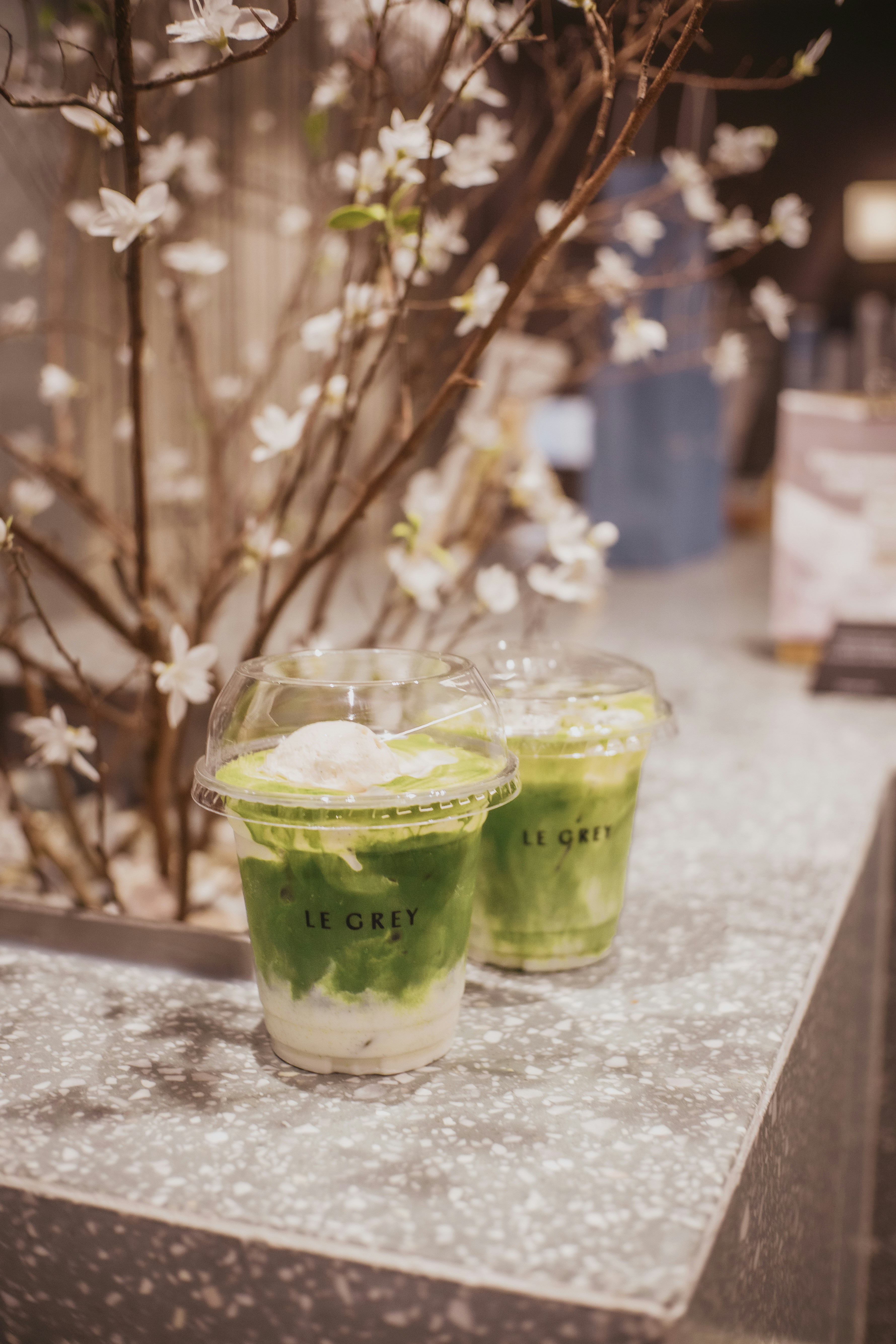 Two iced matcha lattes with scoops of ice cream on a speckled counter