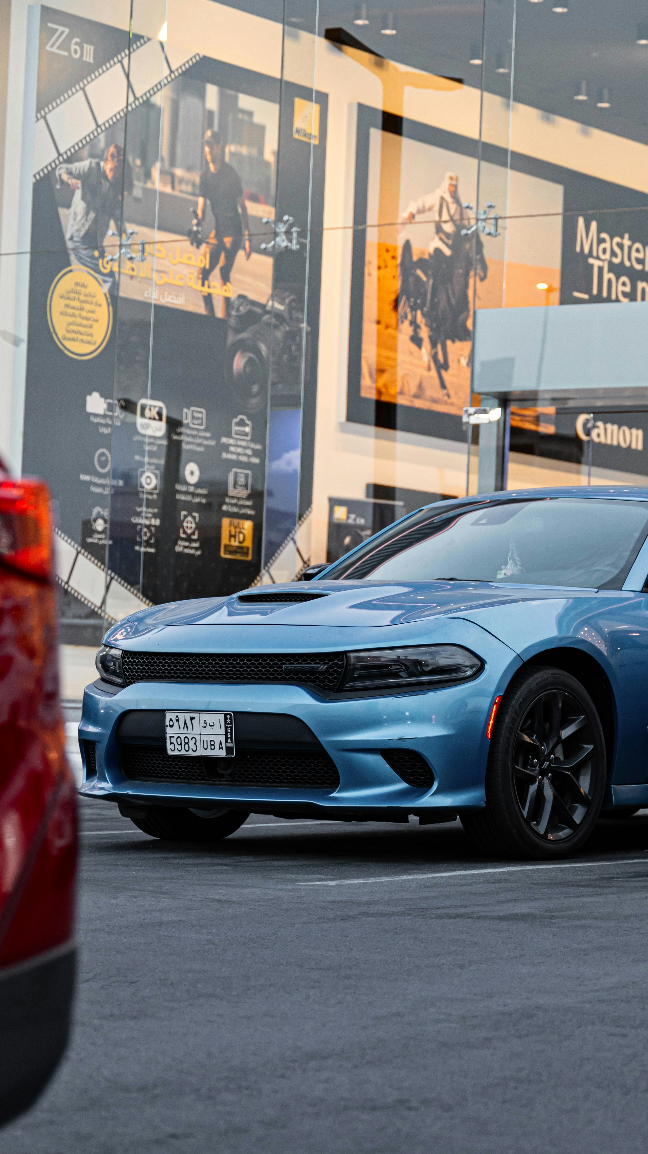 A blue Dodge Charger parked in front of a glass storefront with advertisements