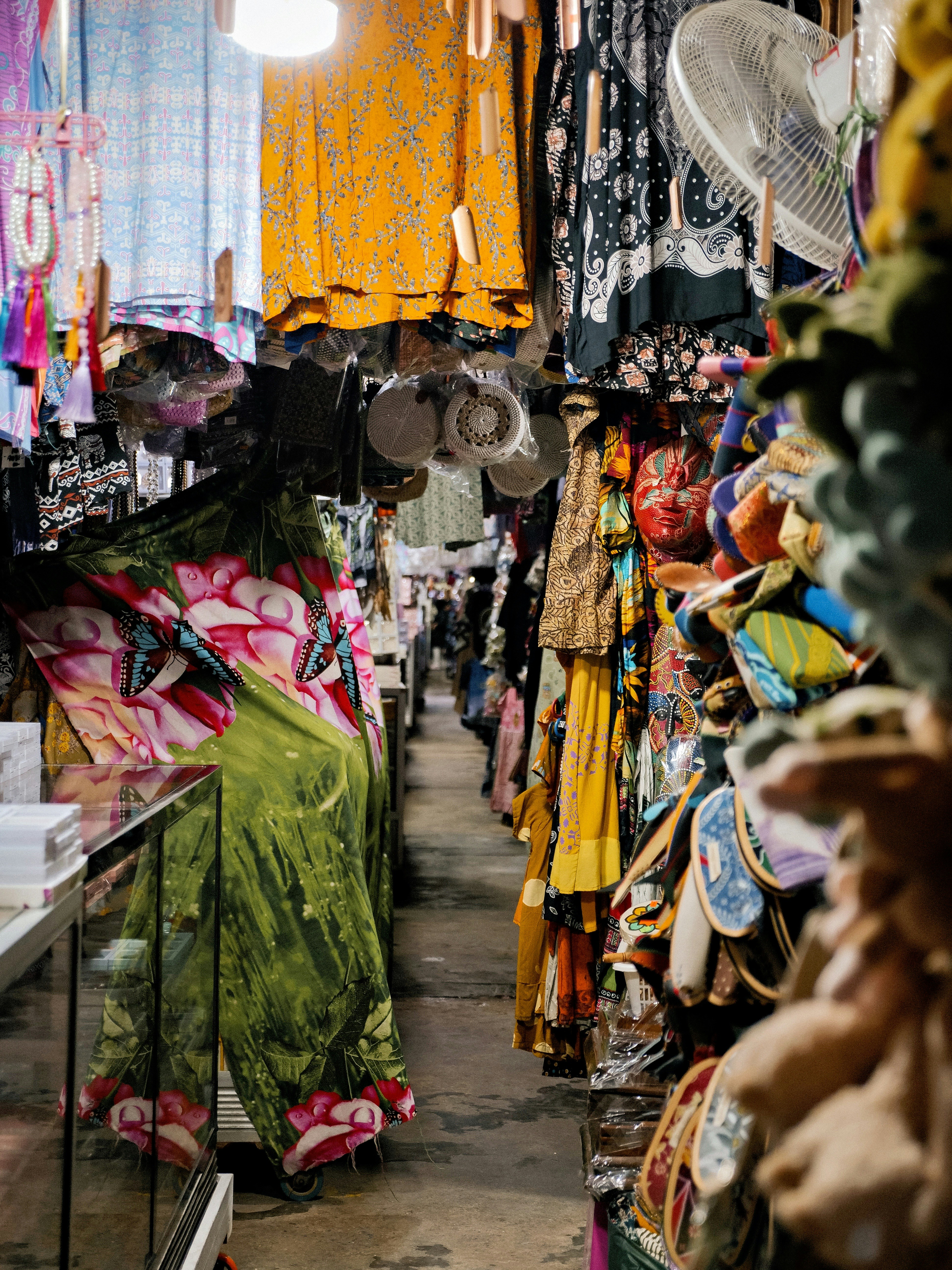 A narrow aisle in a market filled with hanging colorful clothing and accessories