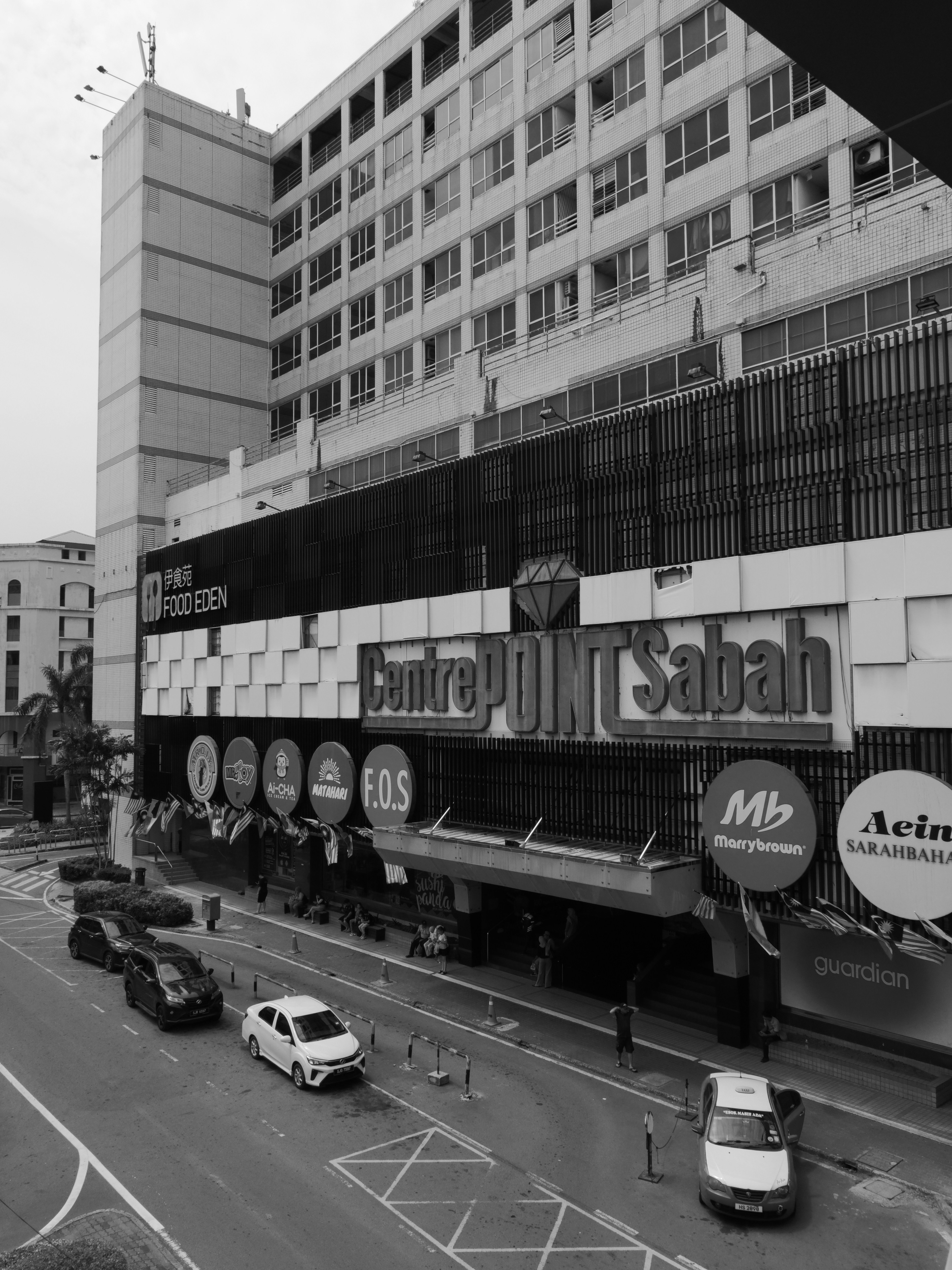 L’extérieur du centre commercial Centre Point Sabah avec divers panneaux de devanture et la circulation dans les chaussures