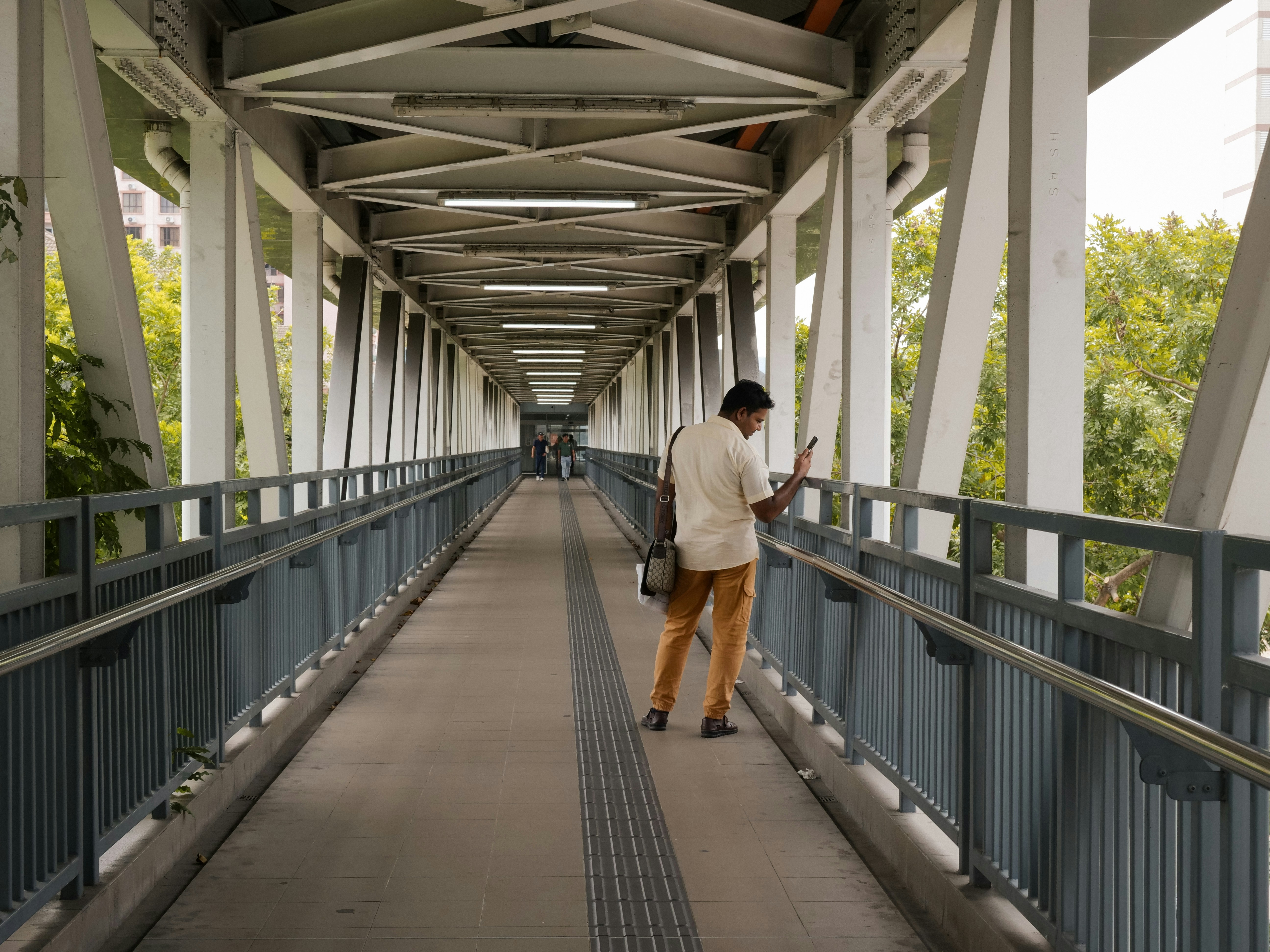 Un homme regardant un smartphone sur une passerelle piétonne couverte