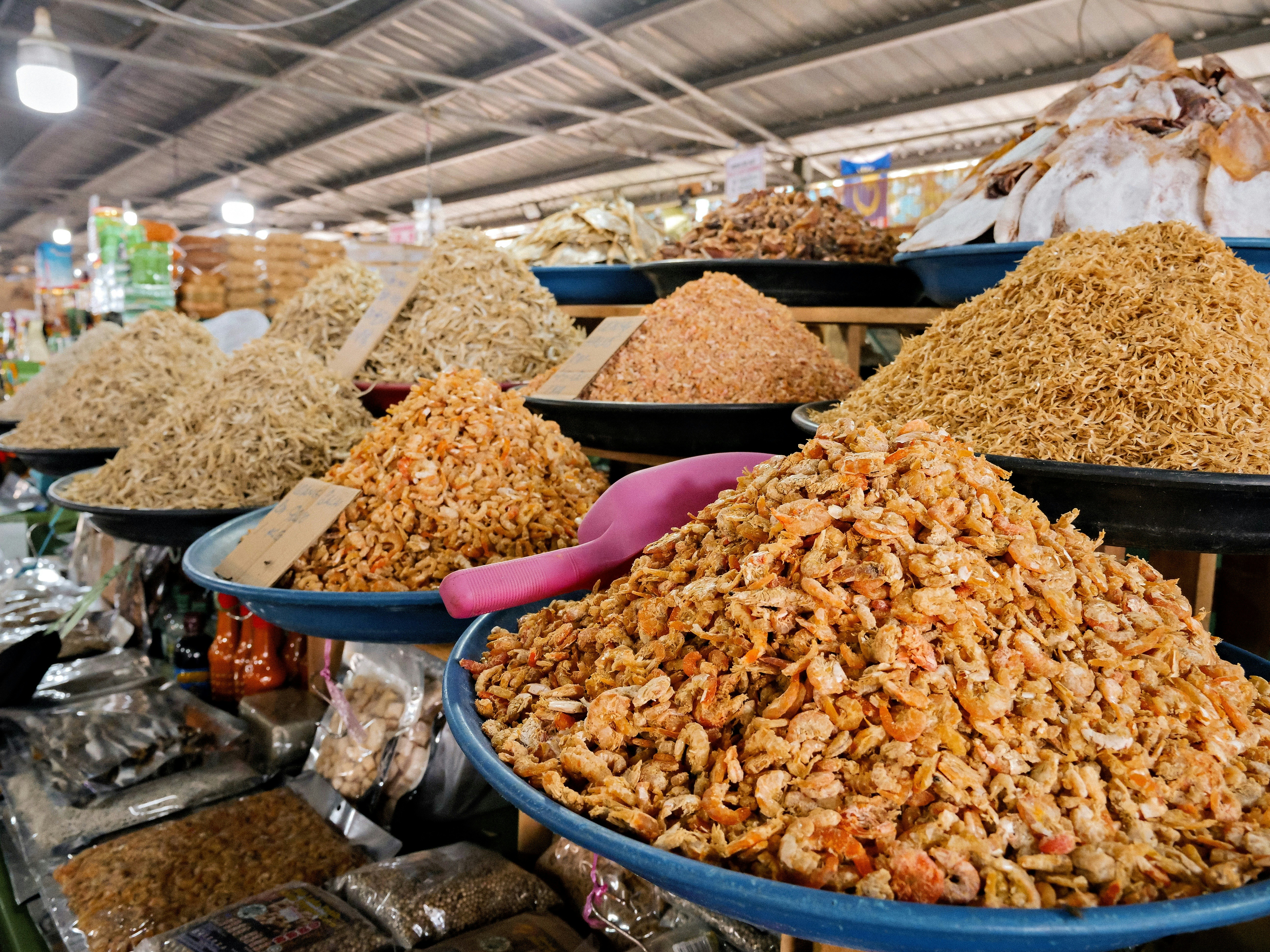 Des tas de crevettes séchées et de petits poissons dans des bocal à un étal de marché
