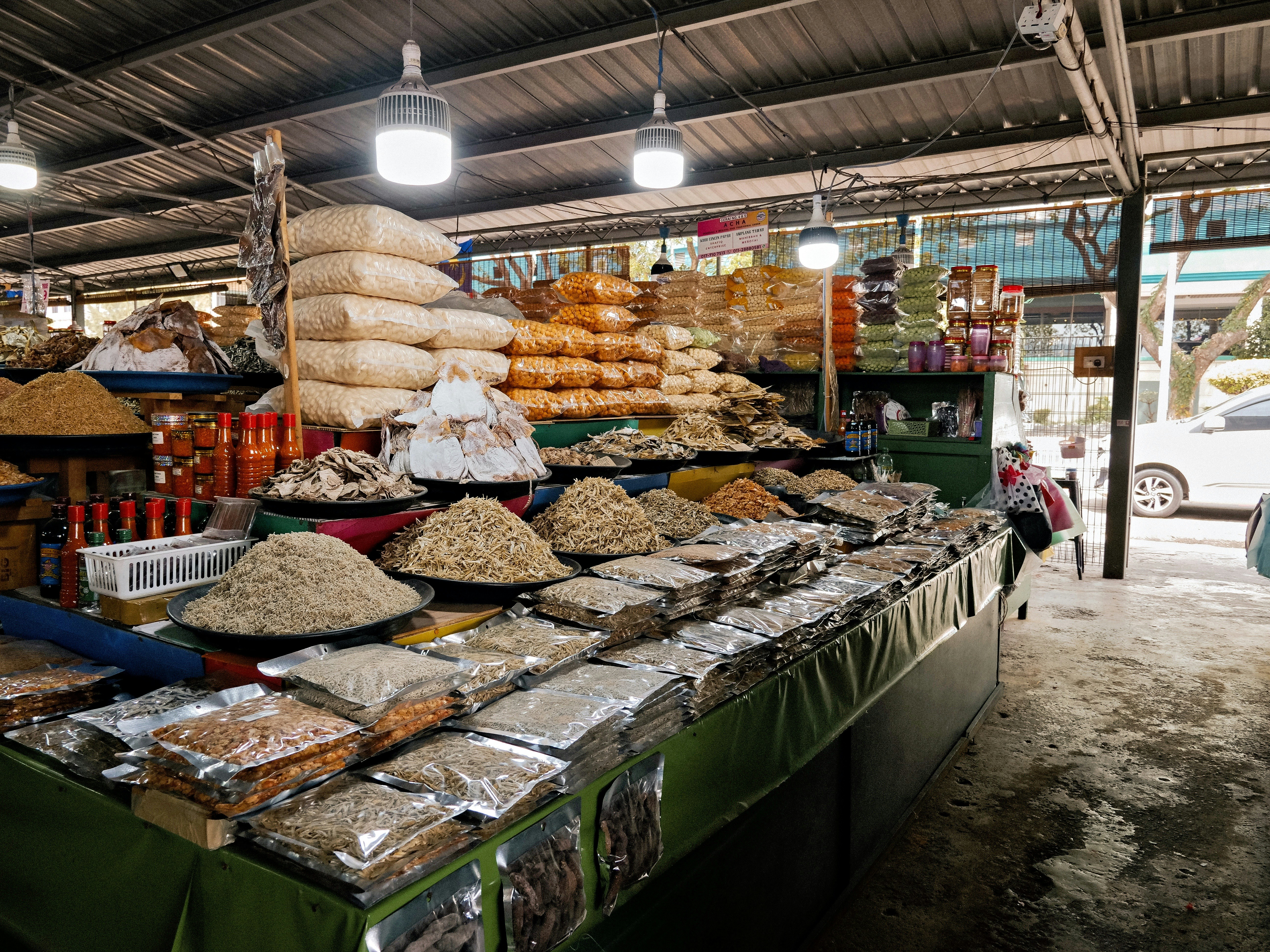 Dried seafood, bottled sauces, and packaged goods arranged beneath hanging lights at a market stall.