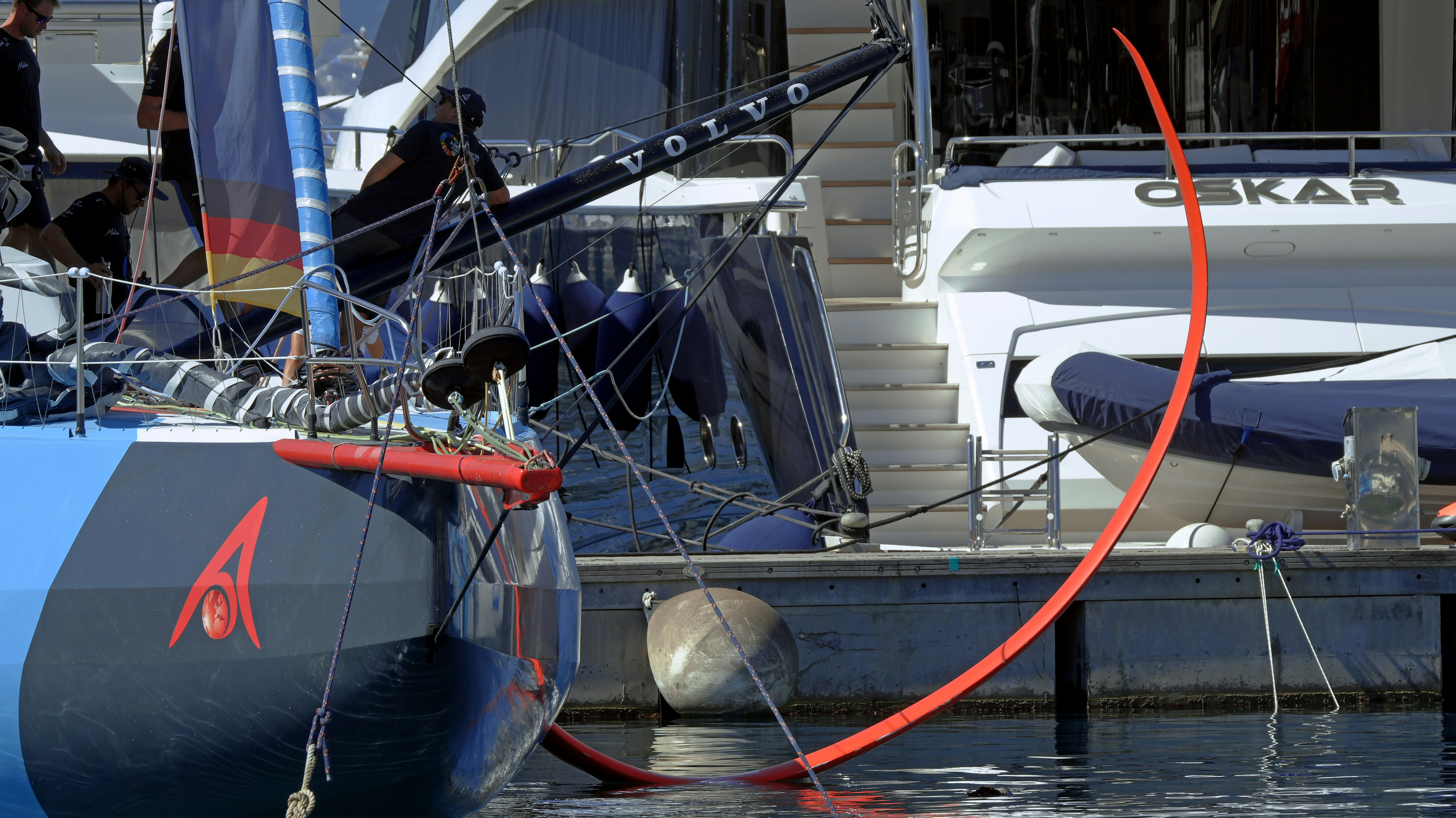 A blue racing sailboat moored beside a white yacht in a marina