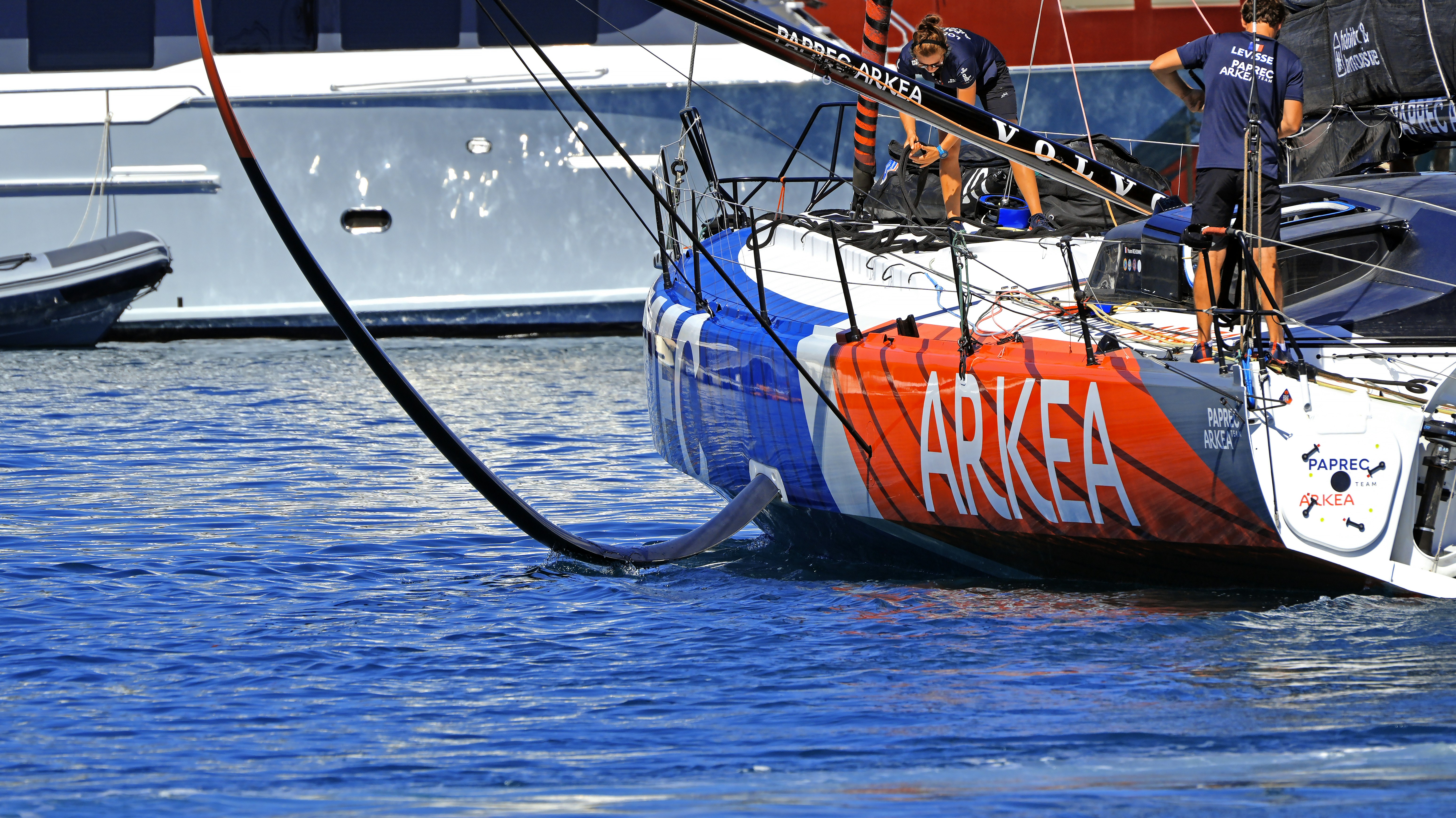 Two people on a racing sailboat with orange and blue hull markings