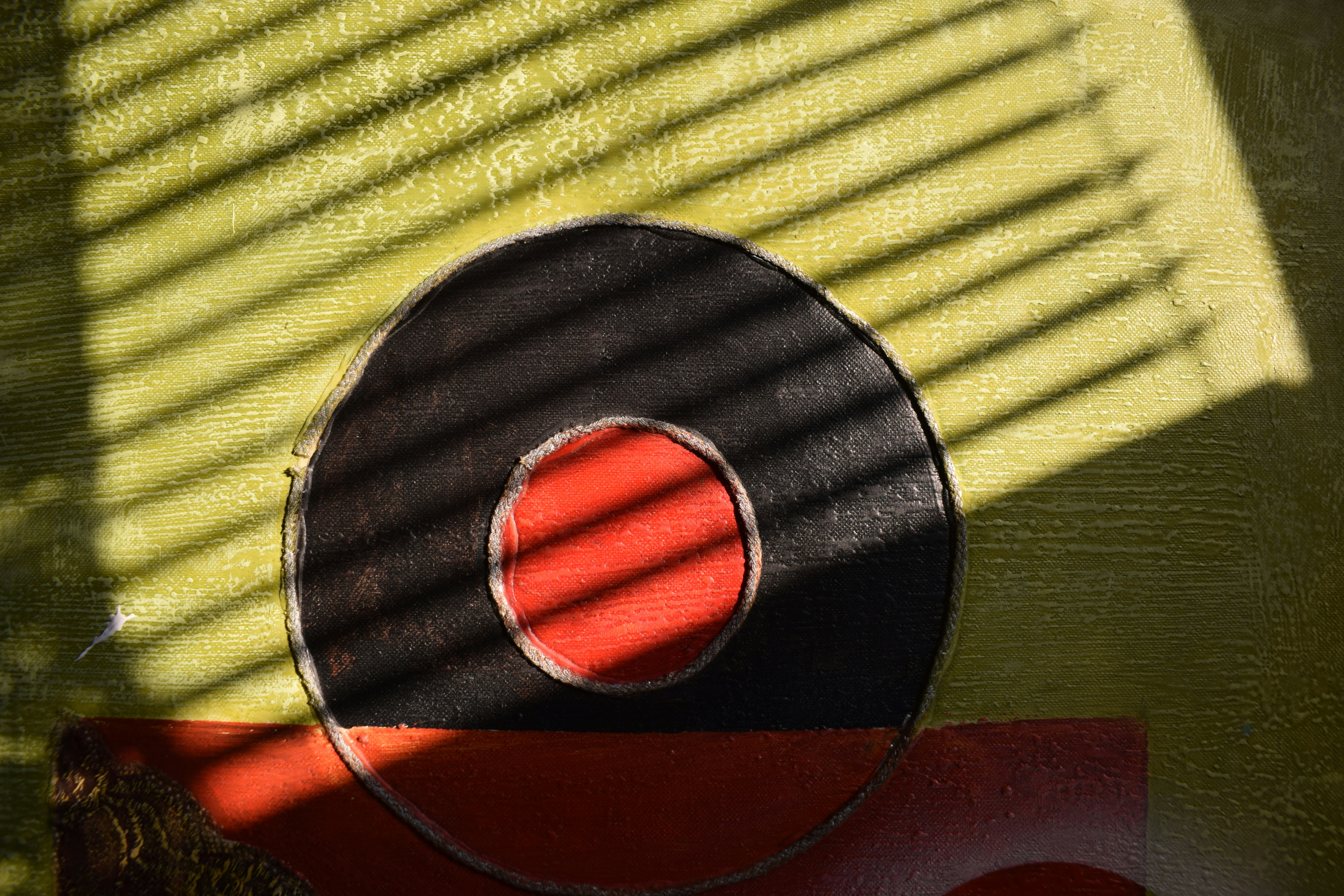 A red circle inside a black circle on a textured yellow surface with striped shadows