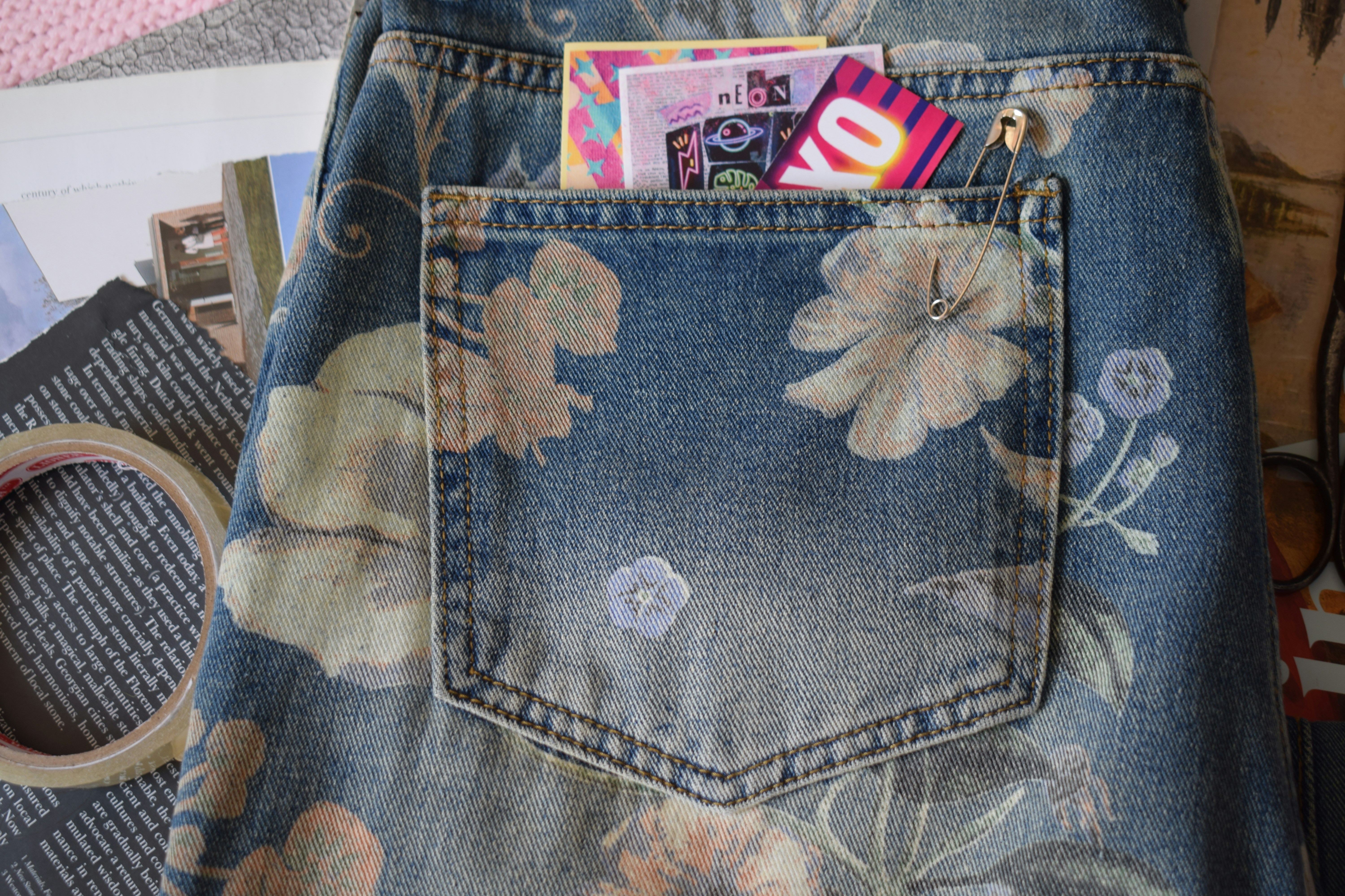 A floral print denim pocket with a safety pin and colorful cards inside