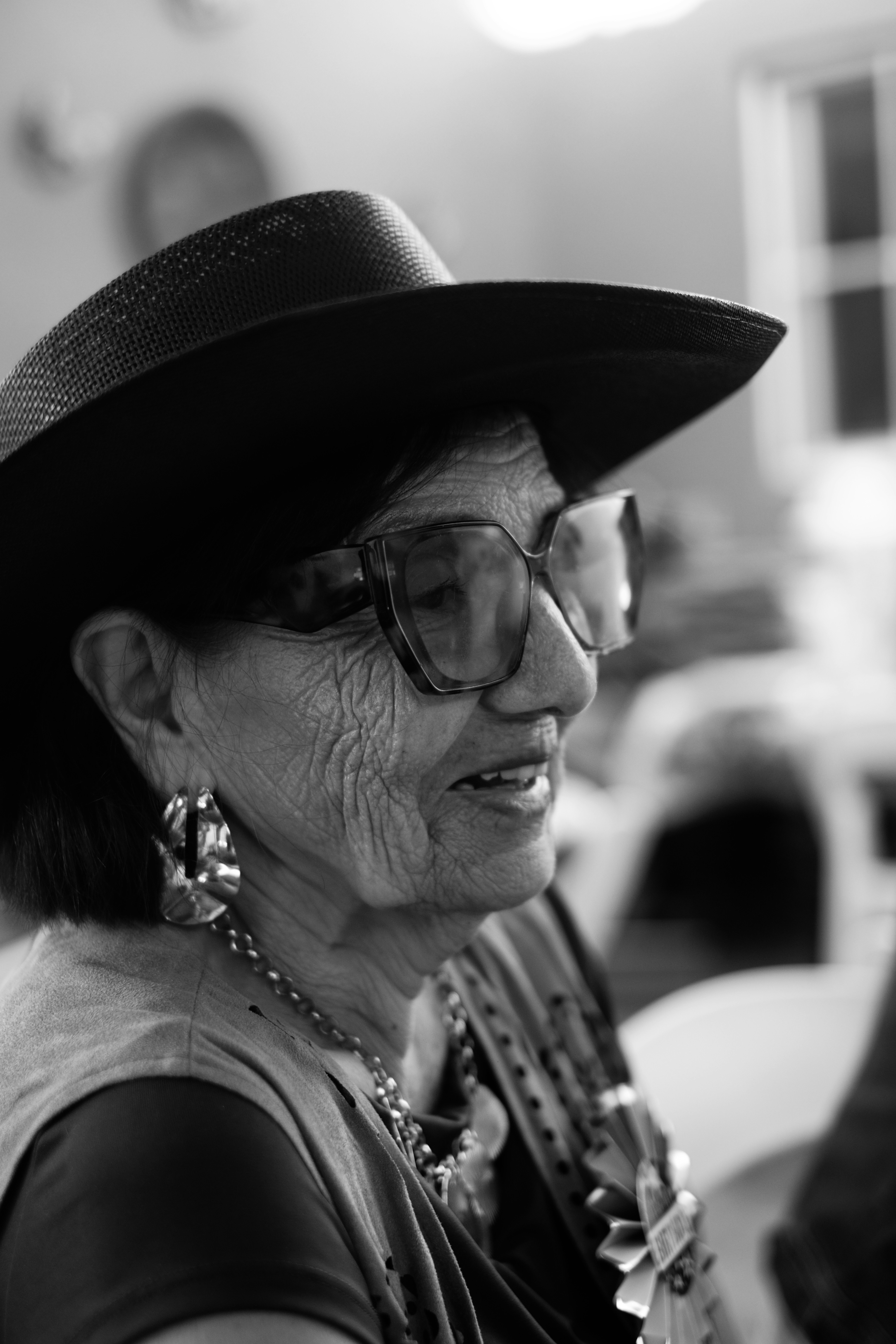 Una anciana con un sombrero de ala ancha, gafas grandes y pendientes llamativos