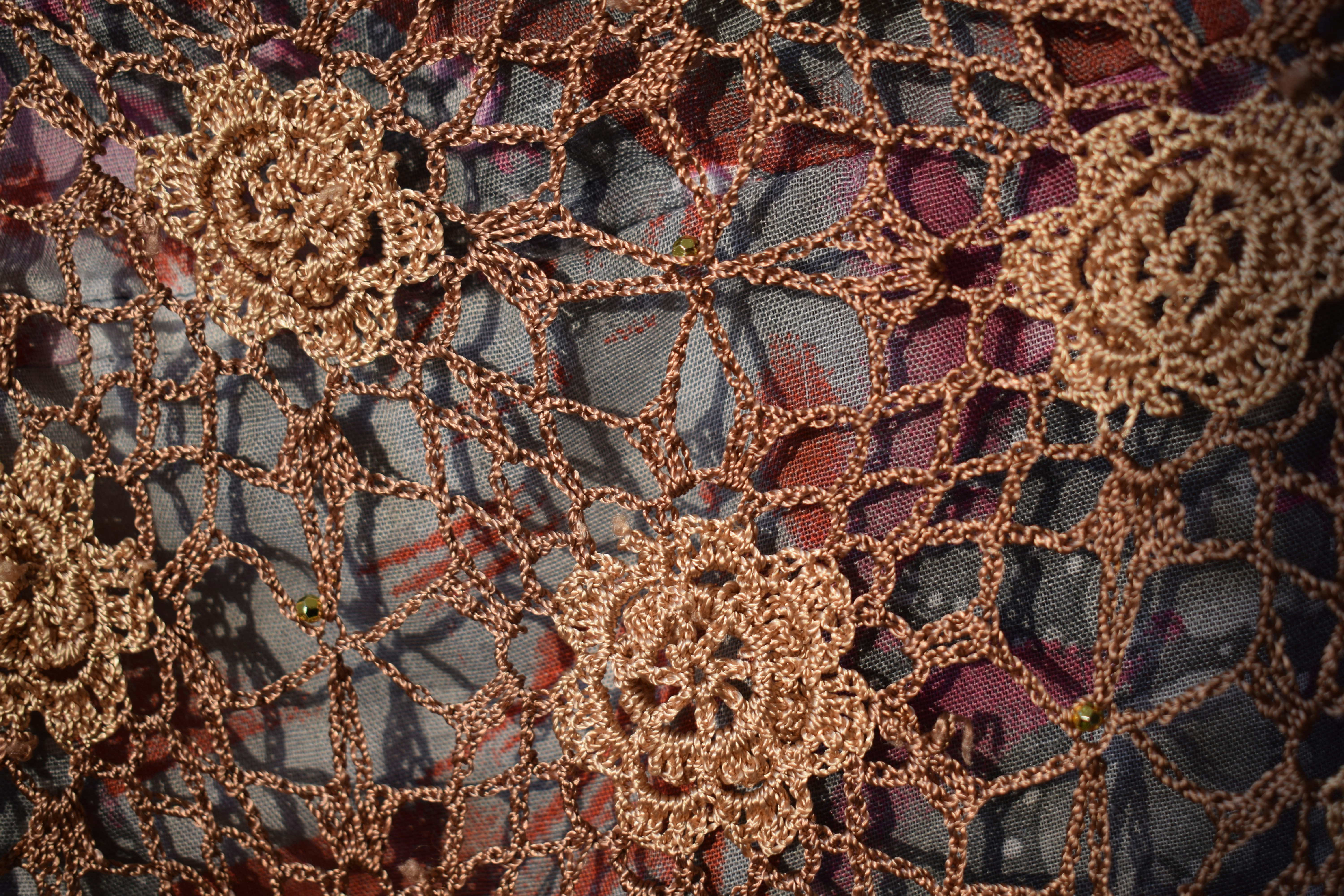 A brown crocheted lace overlay with floral motifs over a patterned fabric