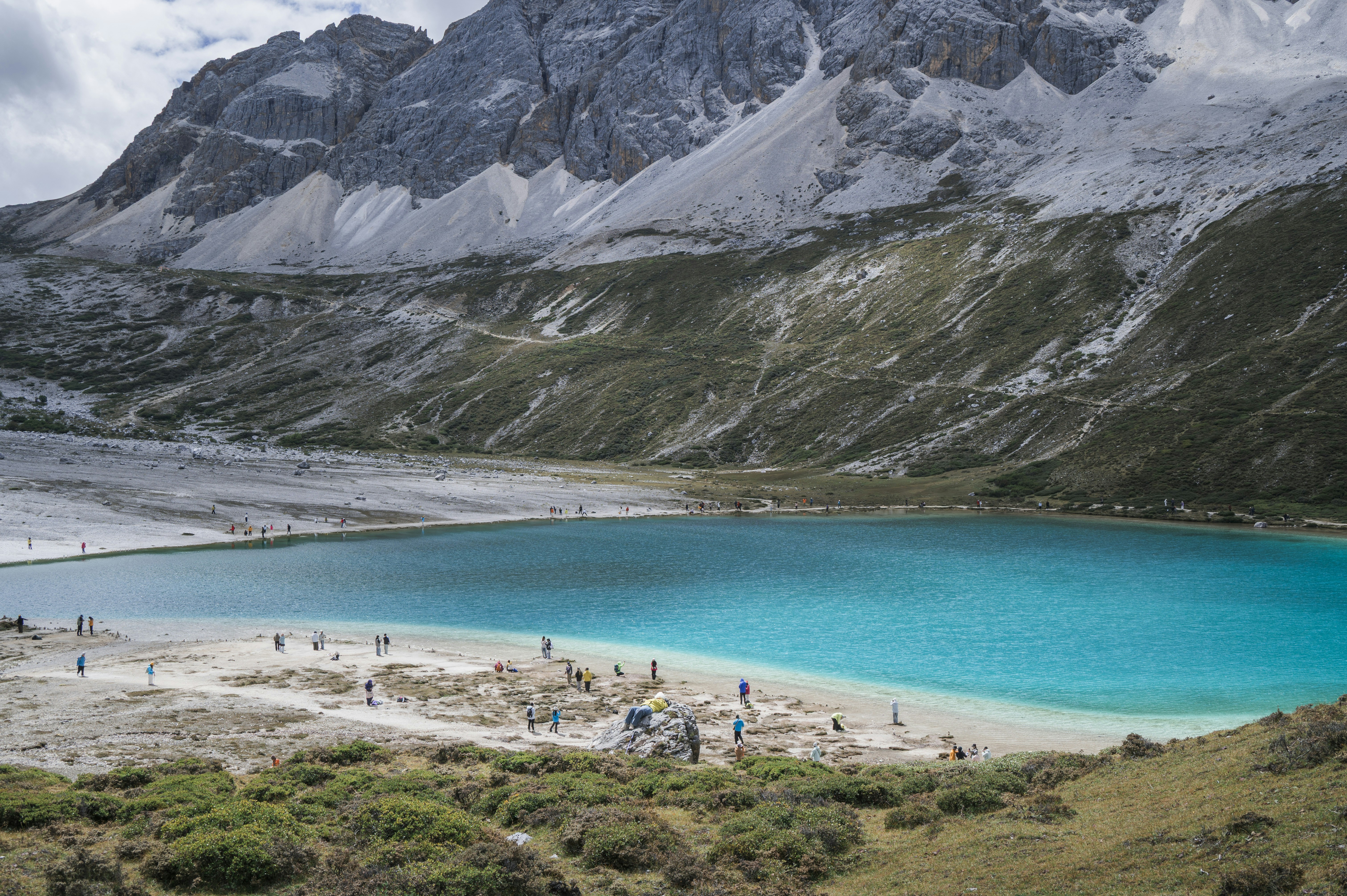 People on the shore of a turquoise glacial lake beneath rugged mountain peaks