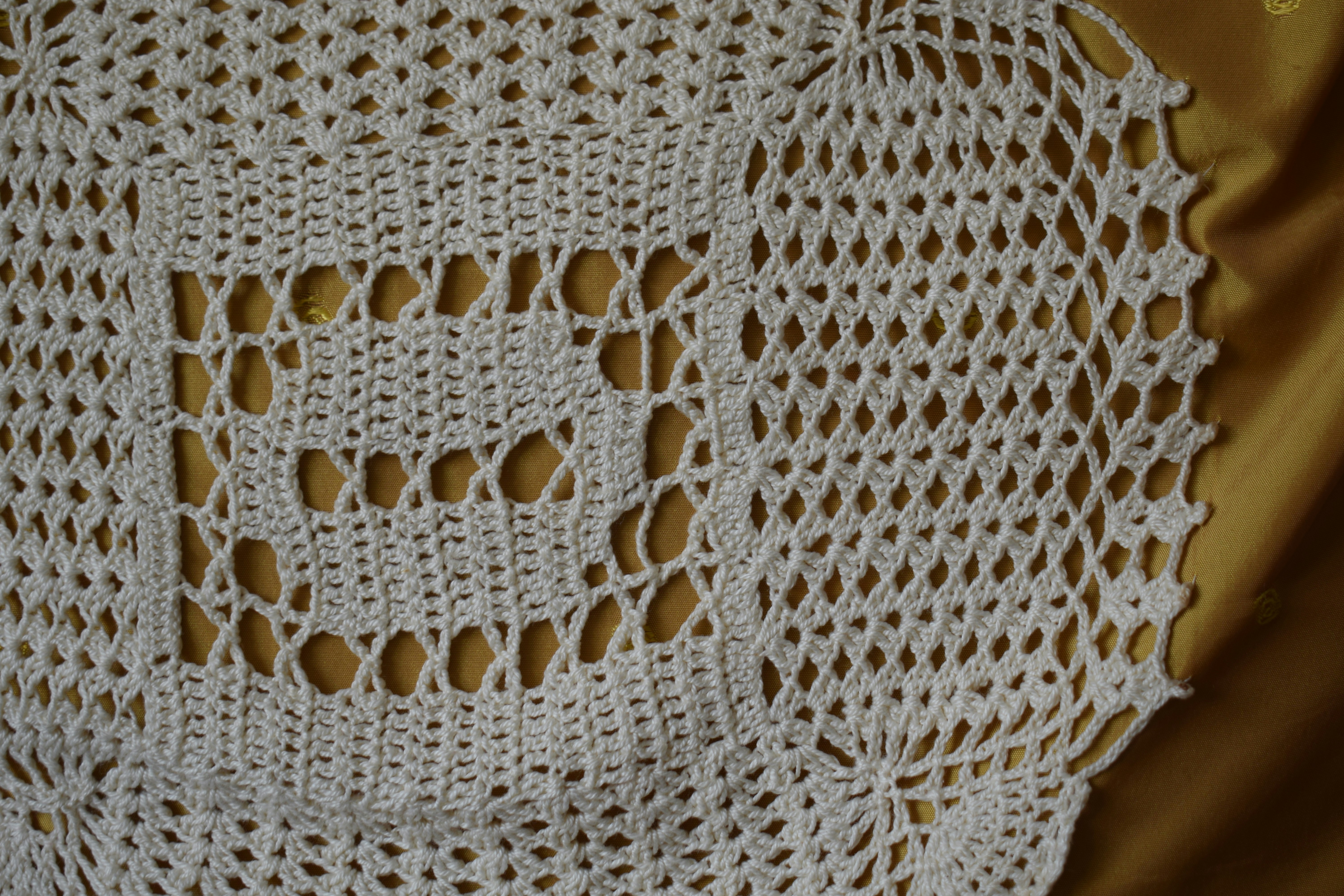 A white crocheted doily with an intricate pattern on a gold fabric background