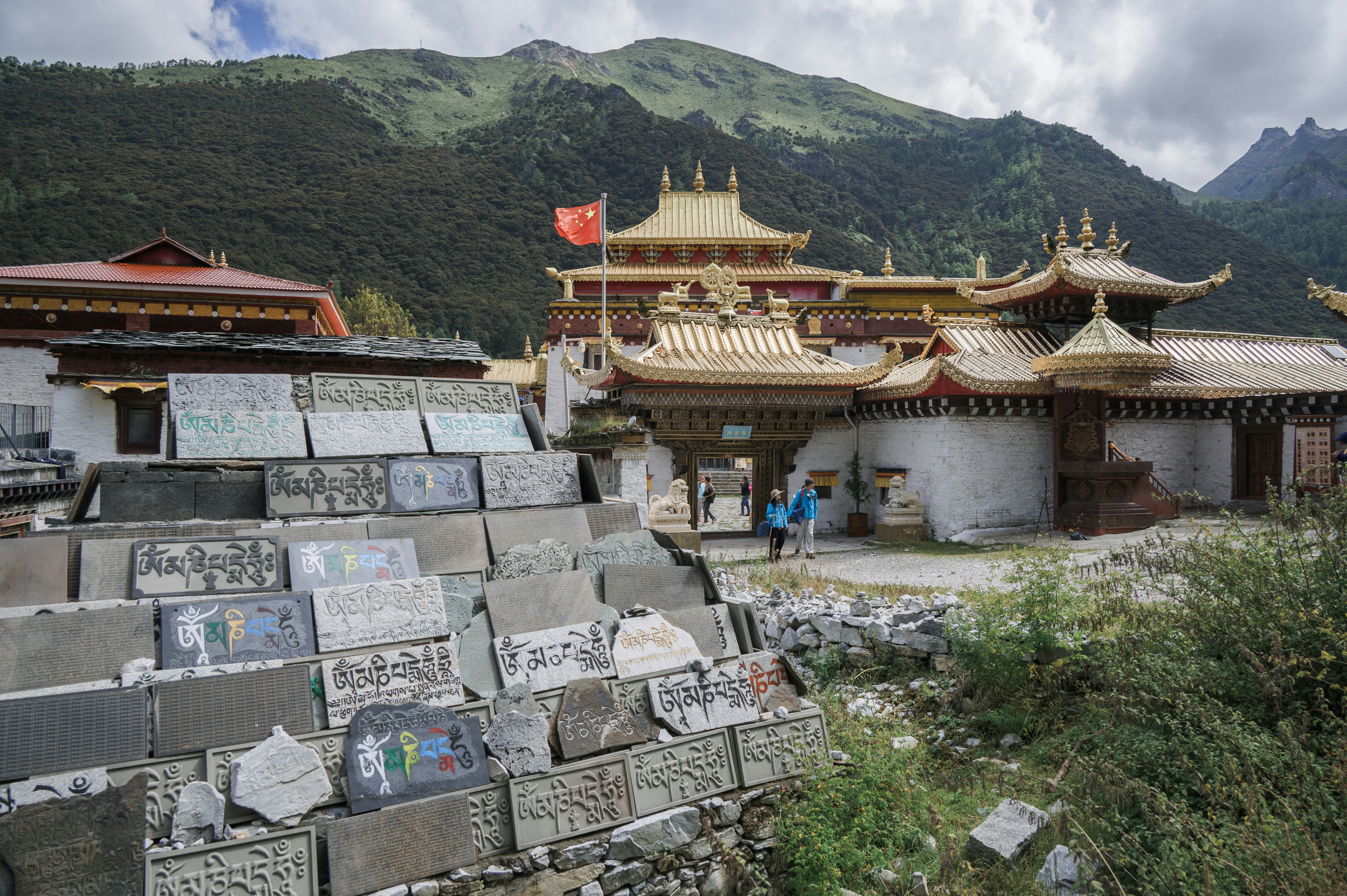 A pile of carved stone prayer tablets before a golden temple in the mountains
