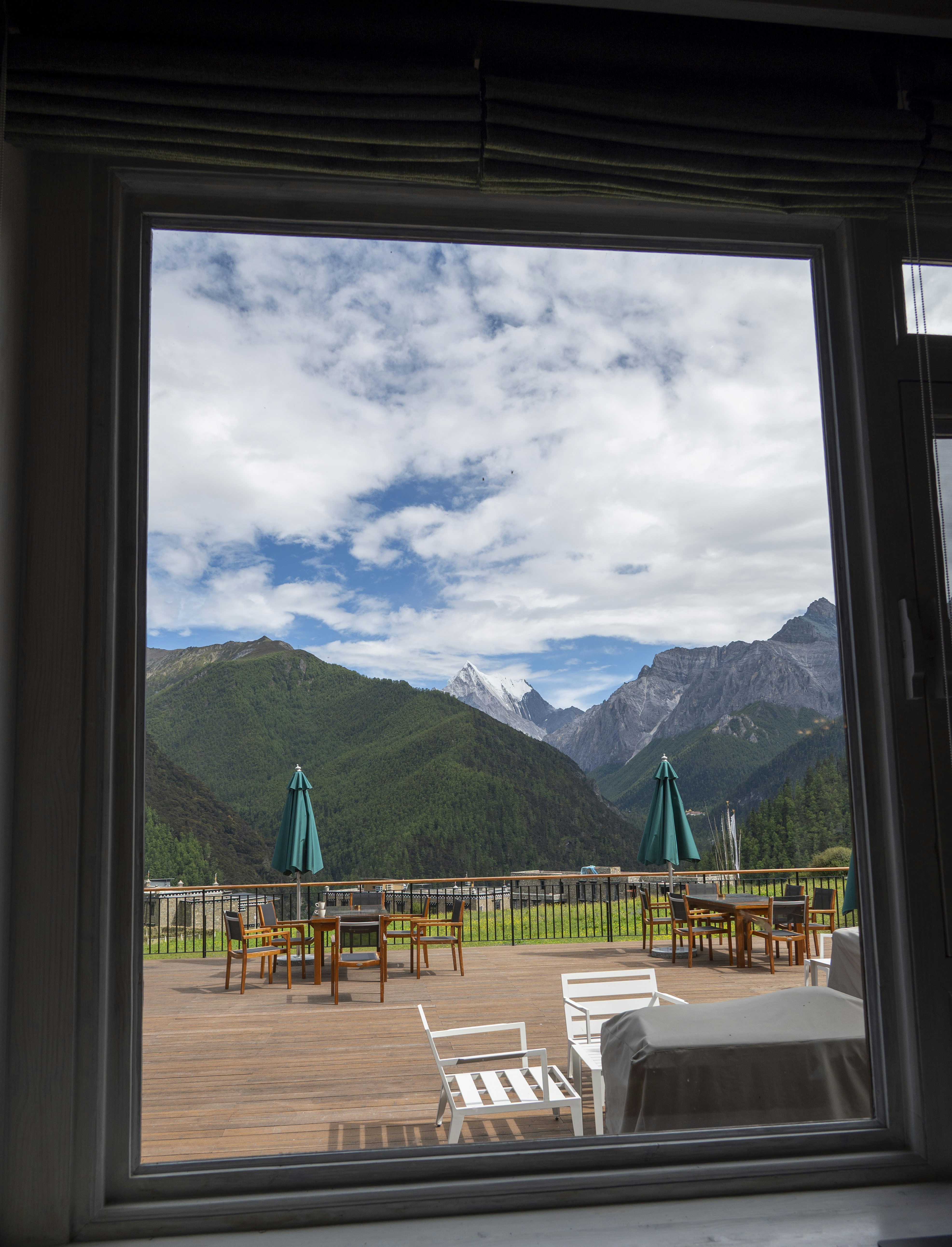 A wooden deck with tables and chairs overlooking green mountains under a cloudy sky