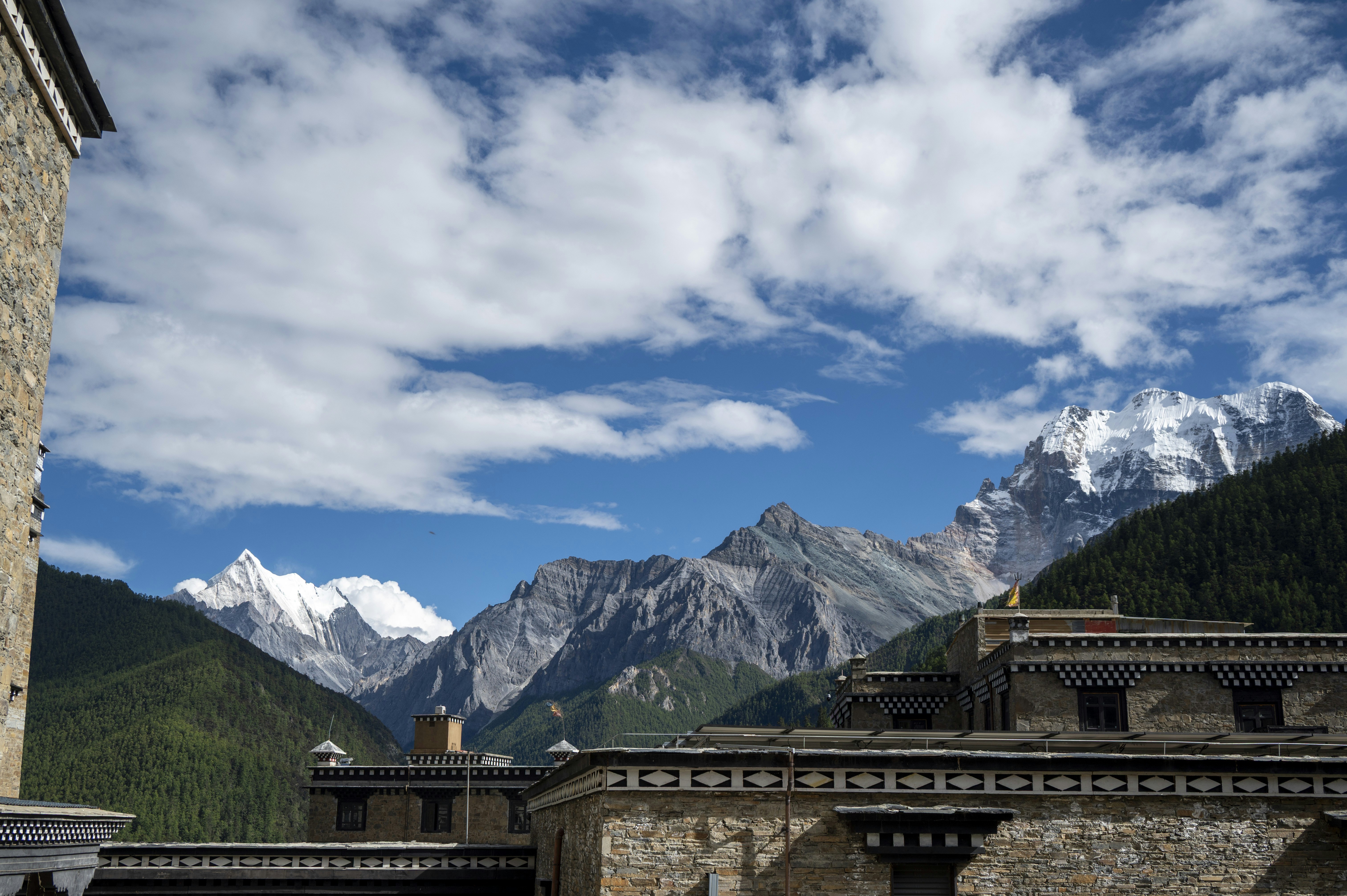 Stone buildings with traditional patterns below snow-capped mountains under a blue sky