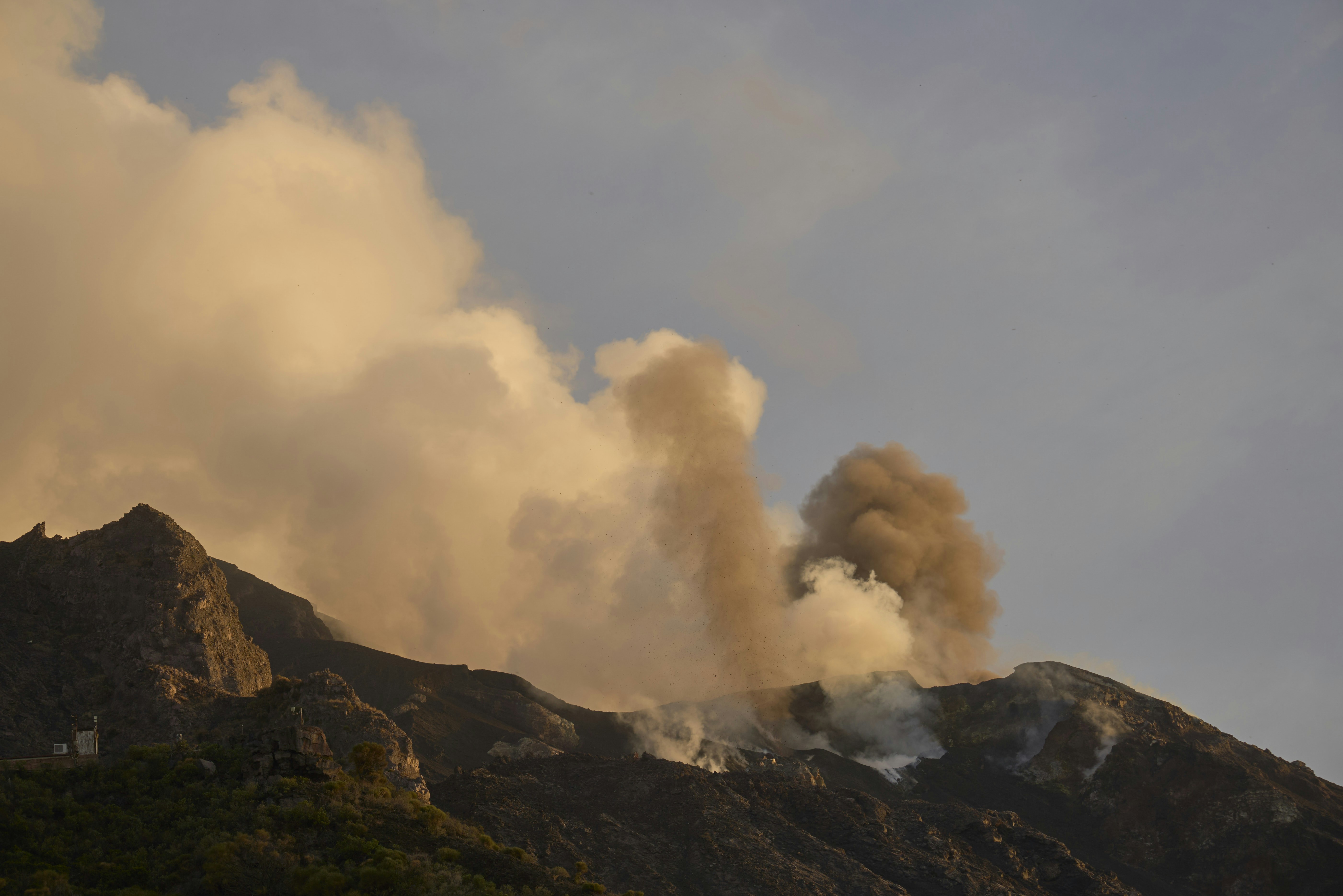 Volcanic ash and steam rising from a dark mountain peak at golden hour