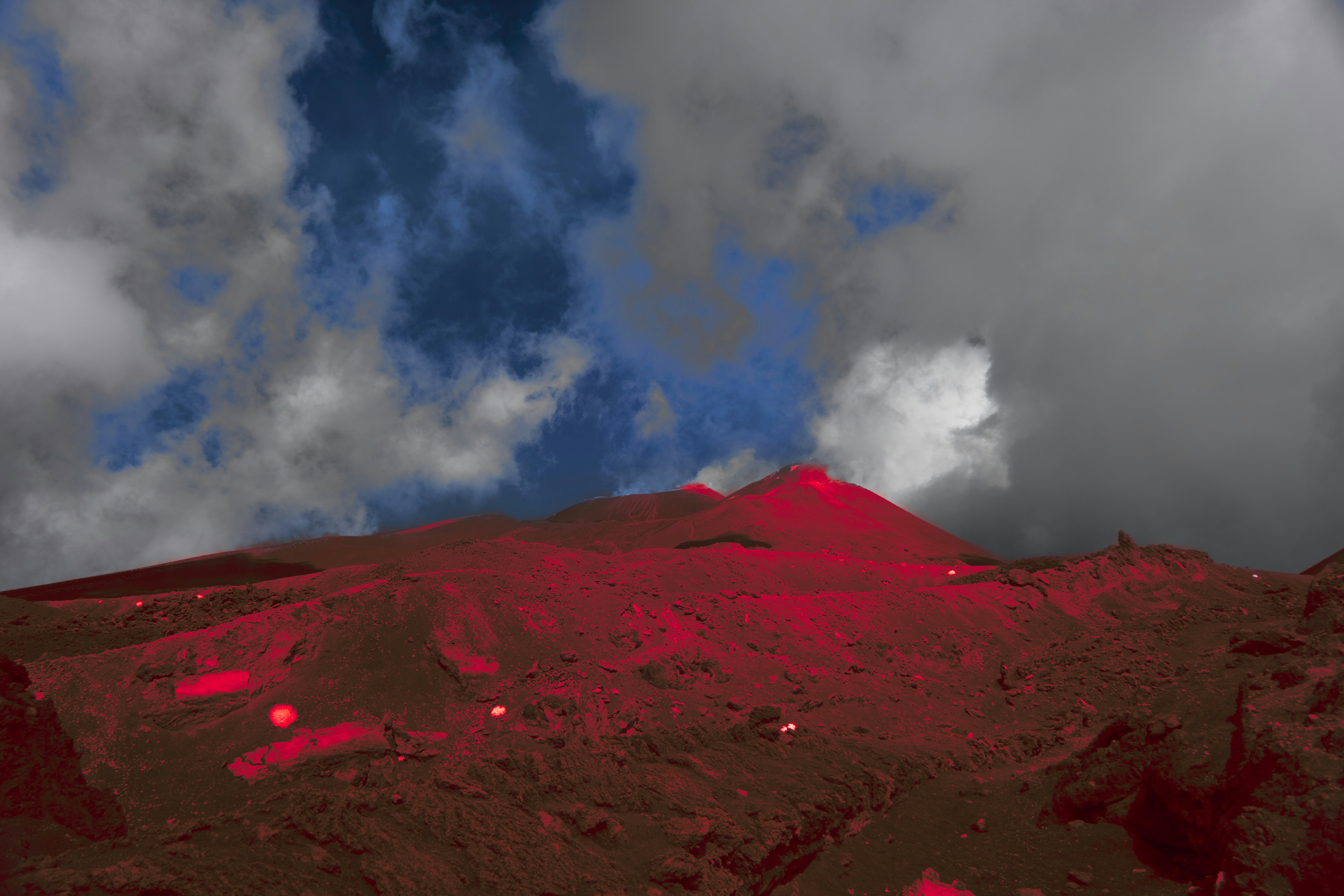 A volcanic mountain slope glowing with intense red light under a cloudy sky