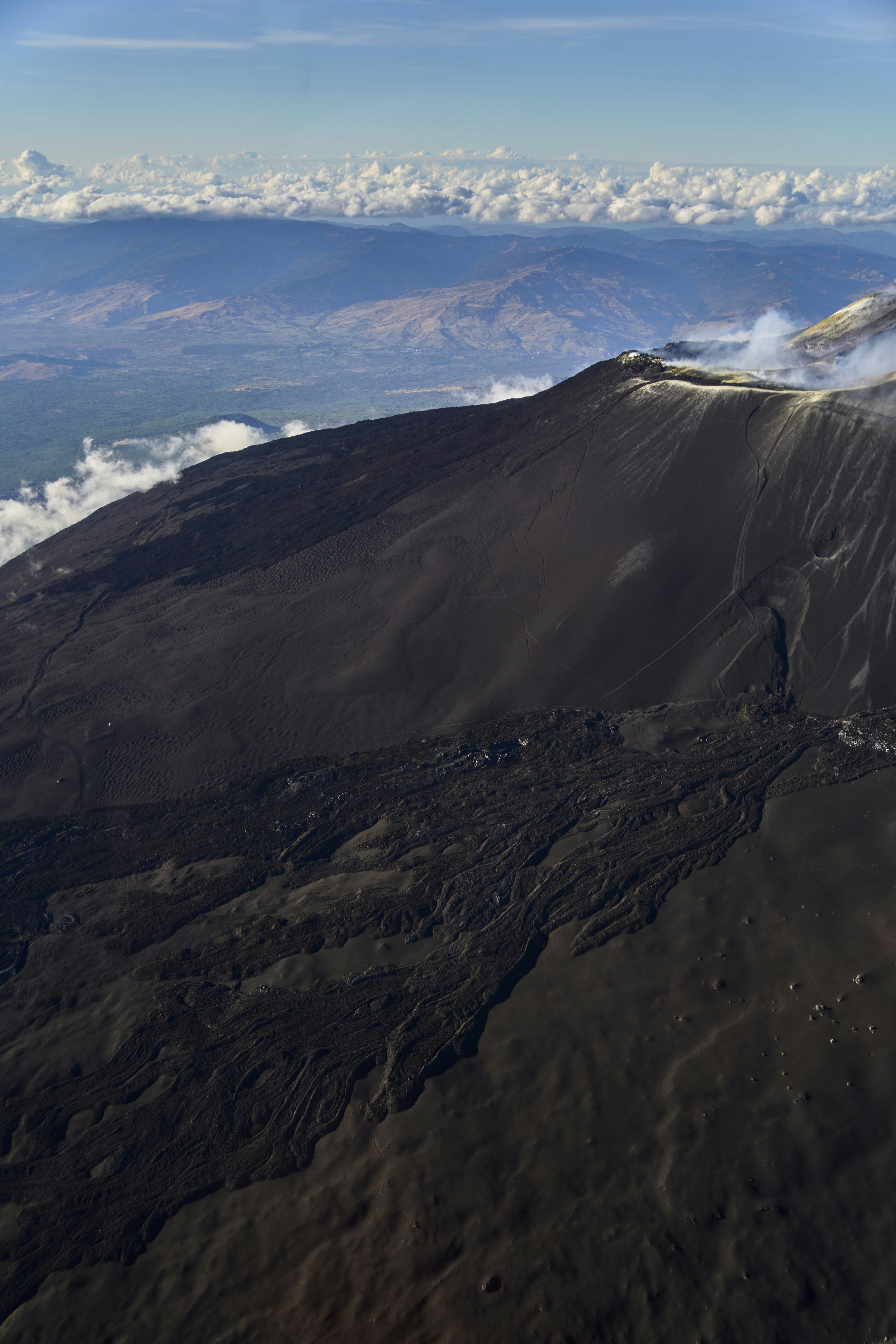 Aerial view of a volcanic crater with dark lava flows and distant mountains