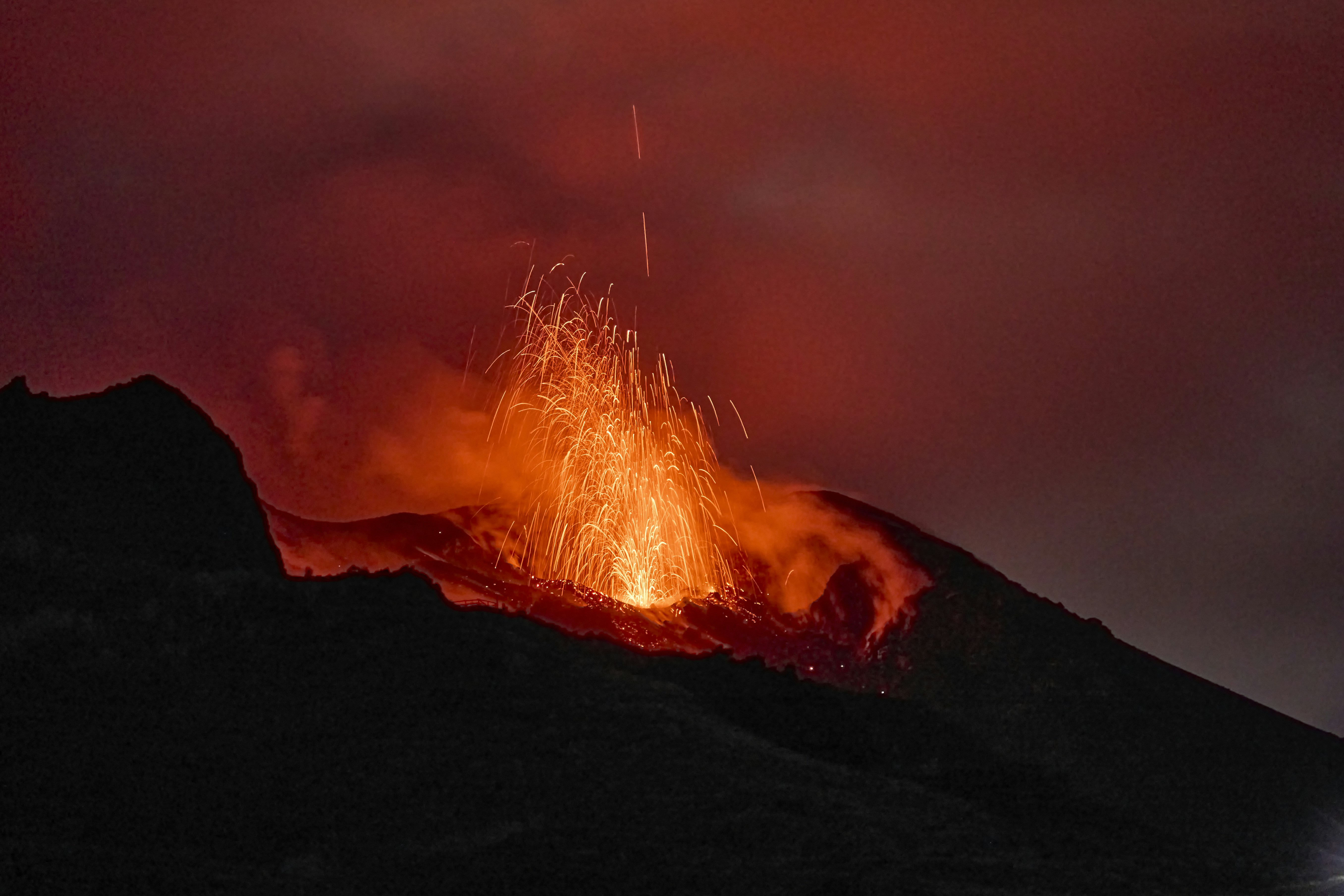 Bright orange lava erupting from a dark volcanic mountain at night