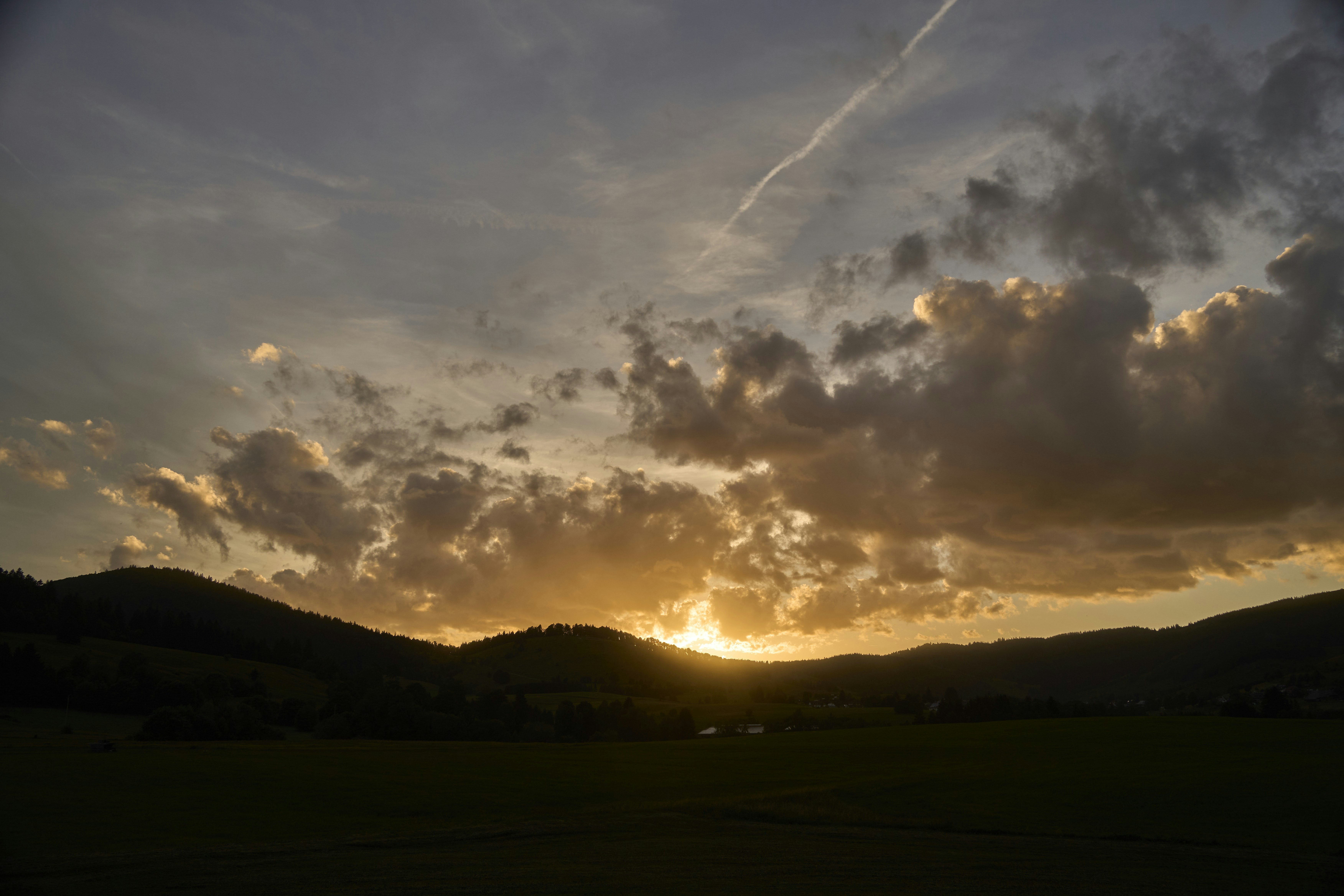 Low sun glowing behind dark hills under a sky with scattered clouds