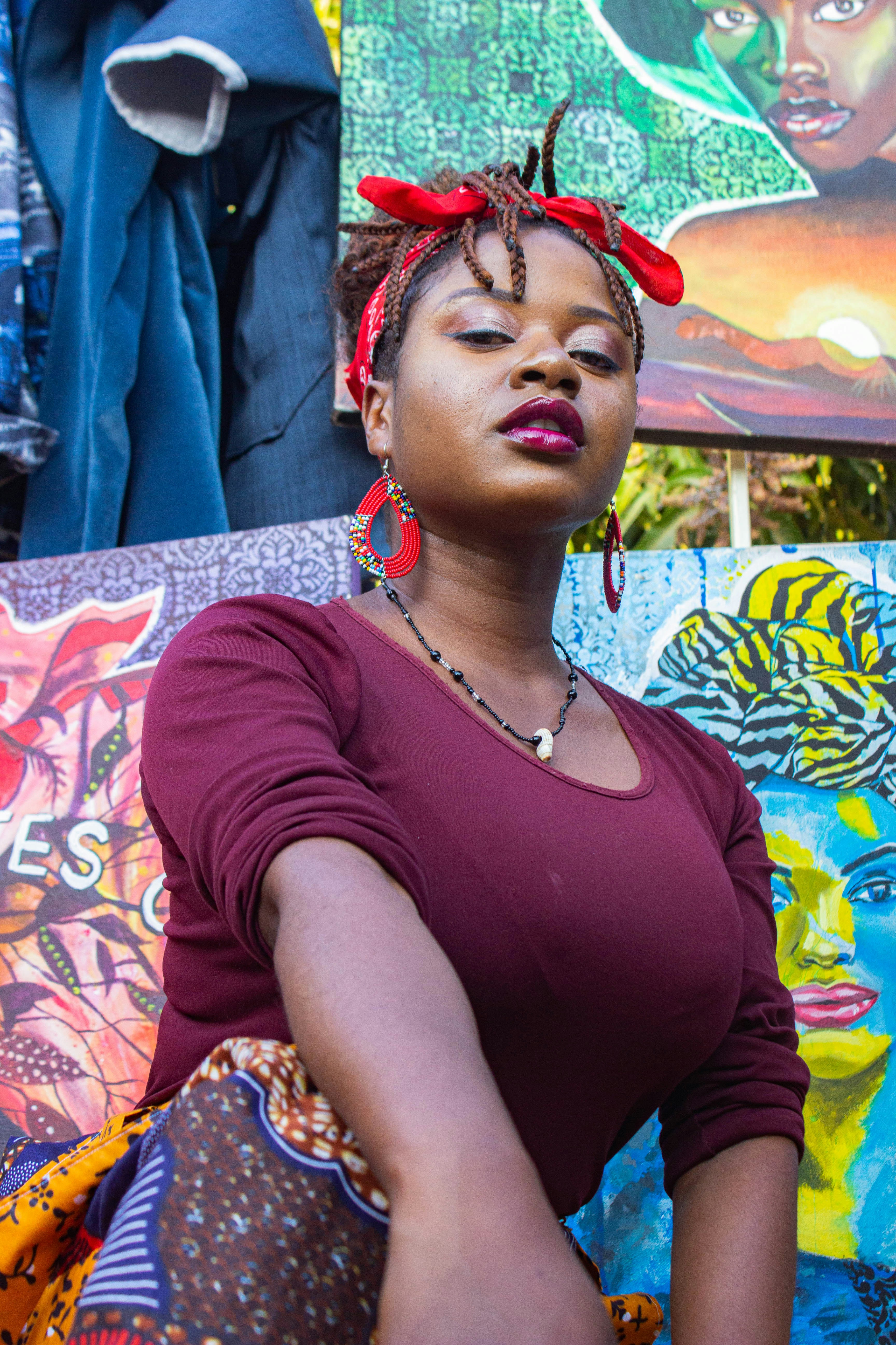 A woman wearing a red bandana and earrings in front of colorful paintings