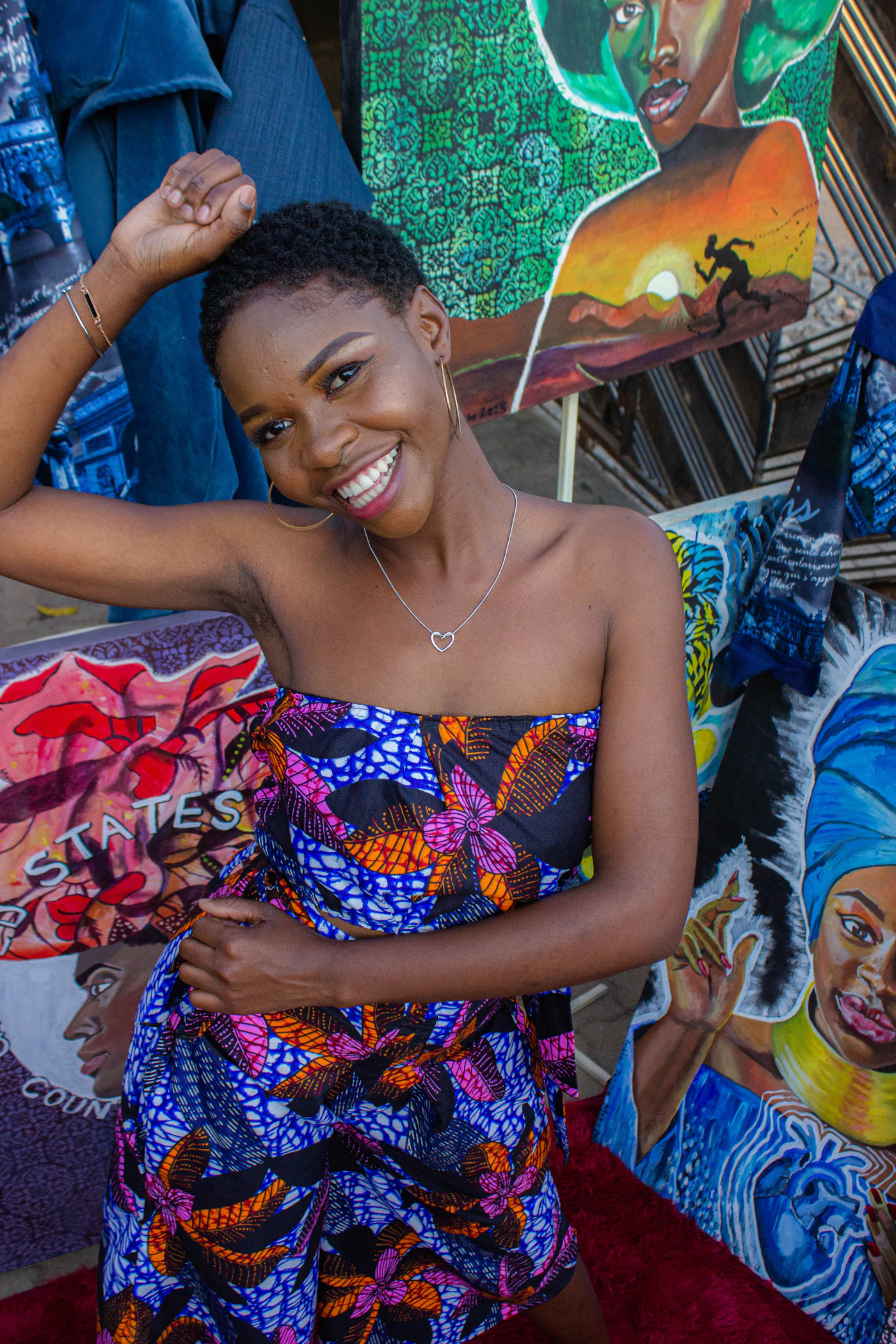 A smiling woman in a colourful patterned outfit standing in front of vibrant colourful prints