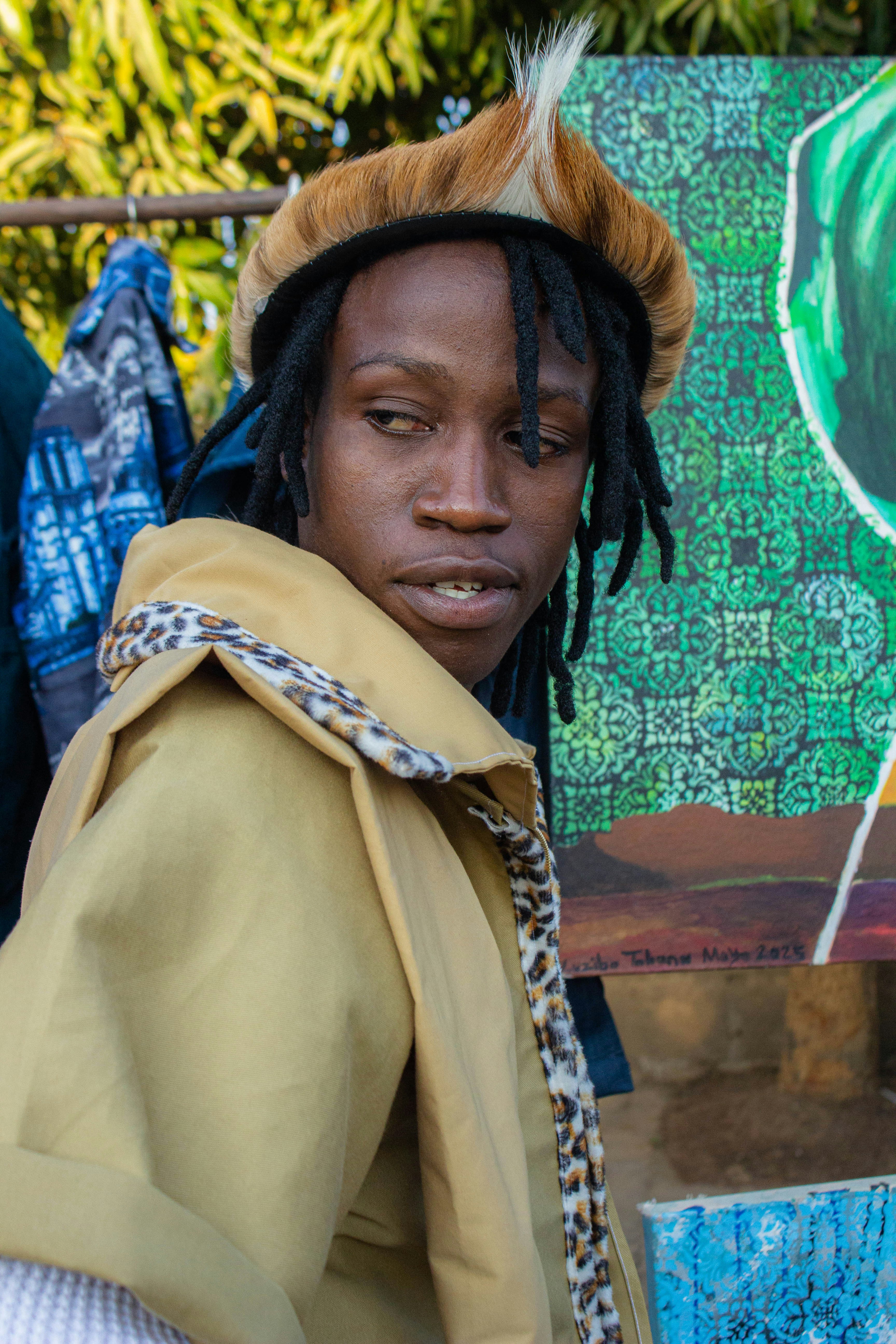 A person with dreadlocks wearing a fur-trimmed hat and tan jacket outdoors