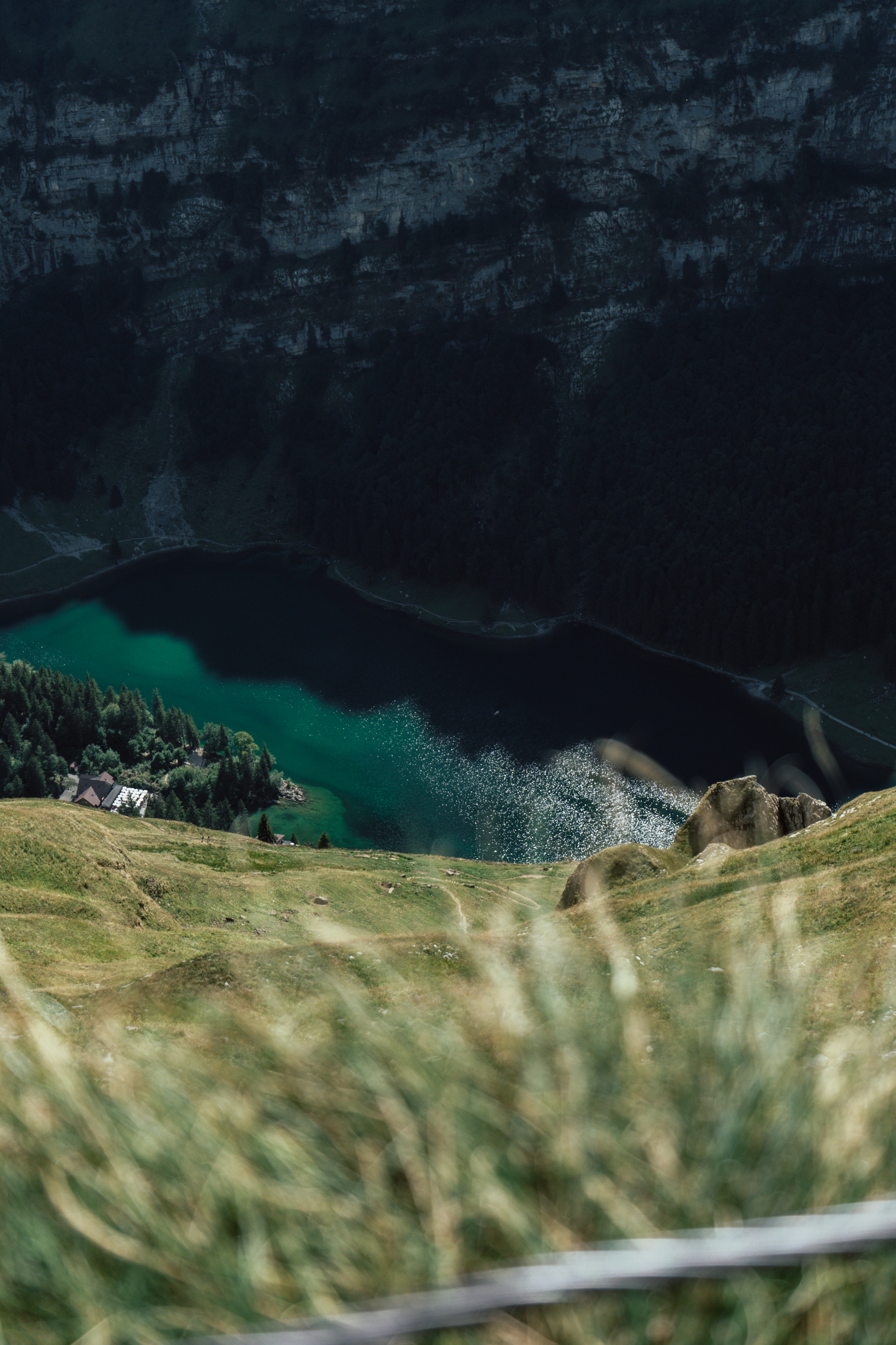 Ein steiler, grasbewachsener Hang mit Blick auf einen tiefgrünen See, eingebettet zwischen felsigen Klippen