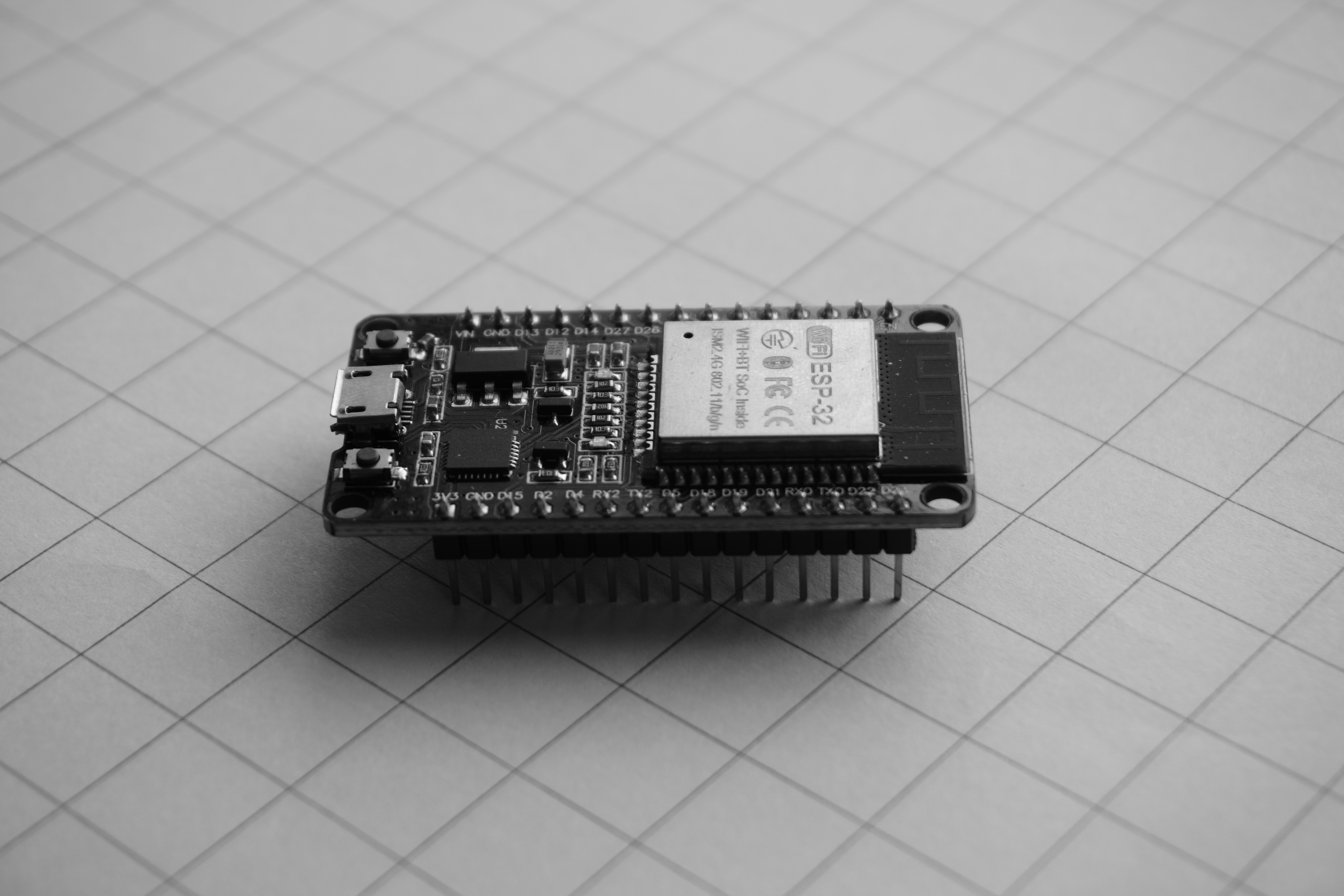 An ESP-32 microcontroller development board on a white grid paper surface