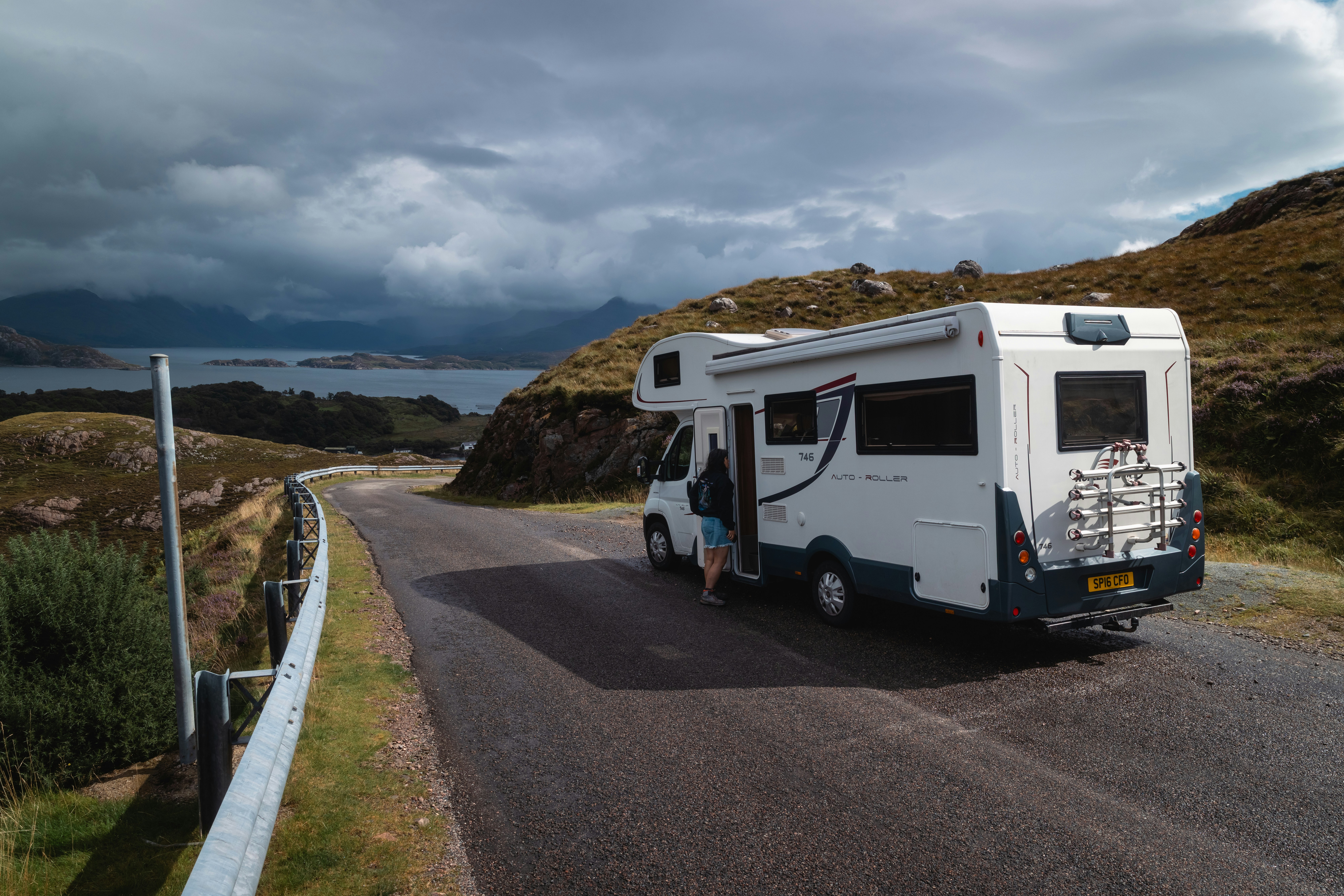 Eine Person, die ein Wohnmobil betritt, das auf einer schmalen Straße neben einer Küstenlandschaft geparkt ist