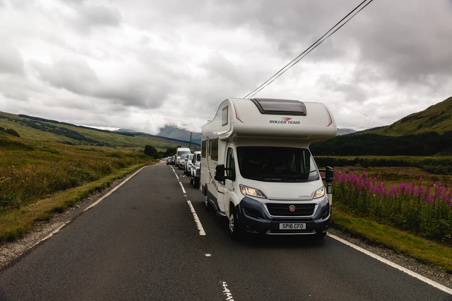 A white motorhome leading a line of cars on a country road