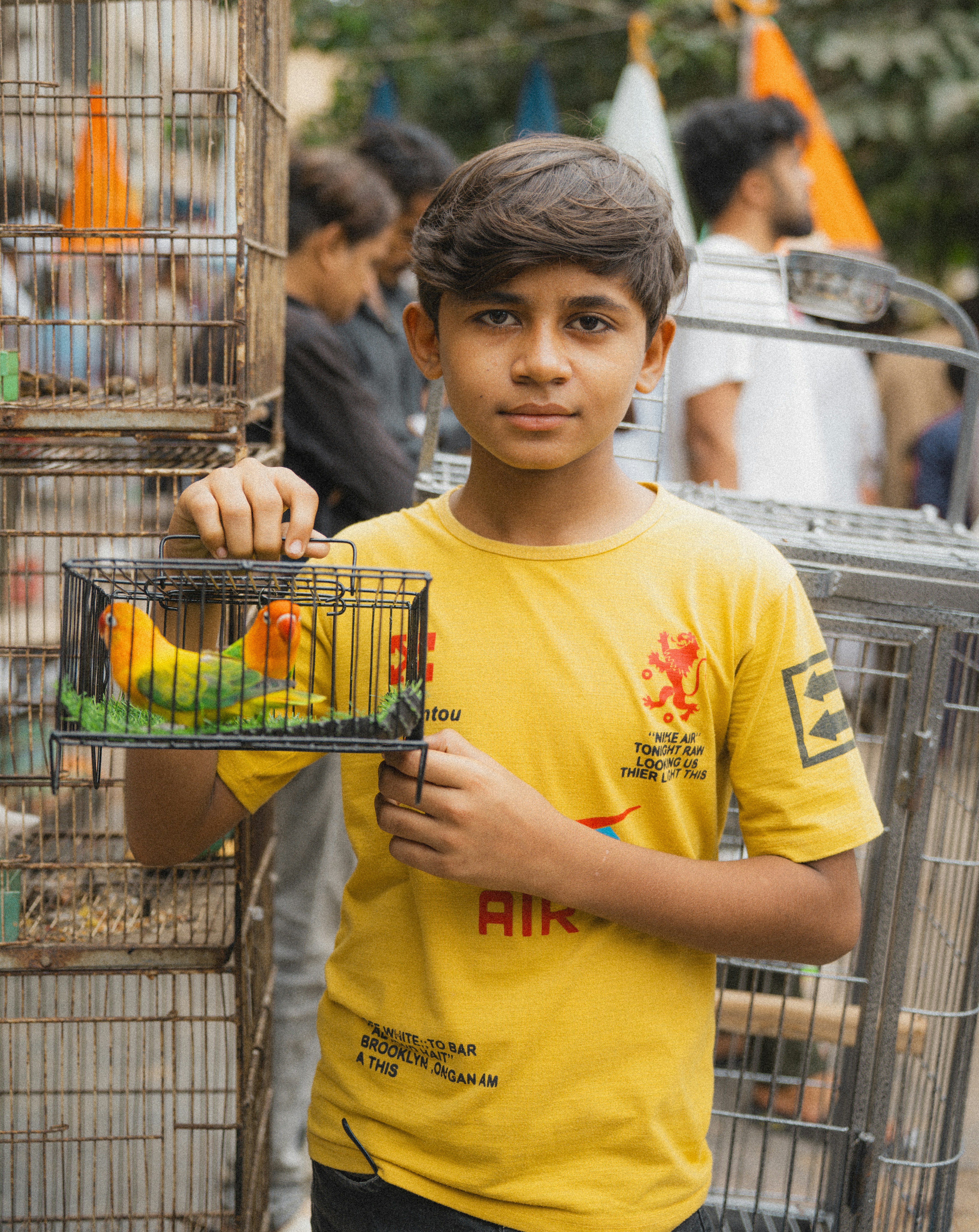 Um garoto de camiseta amarela segurando uma pequena gaiola com dois pombinhos
