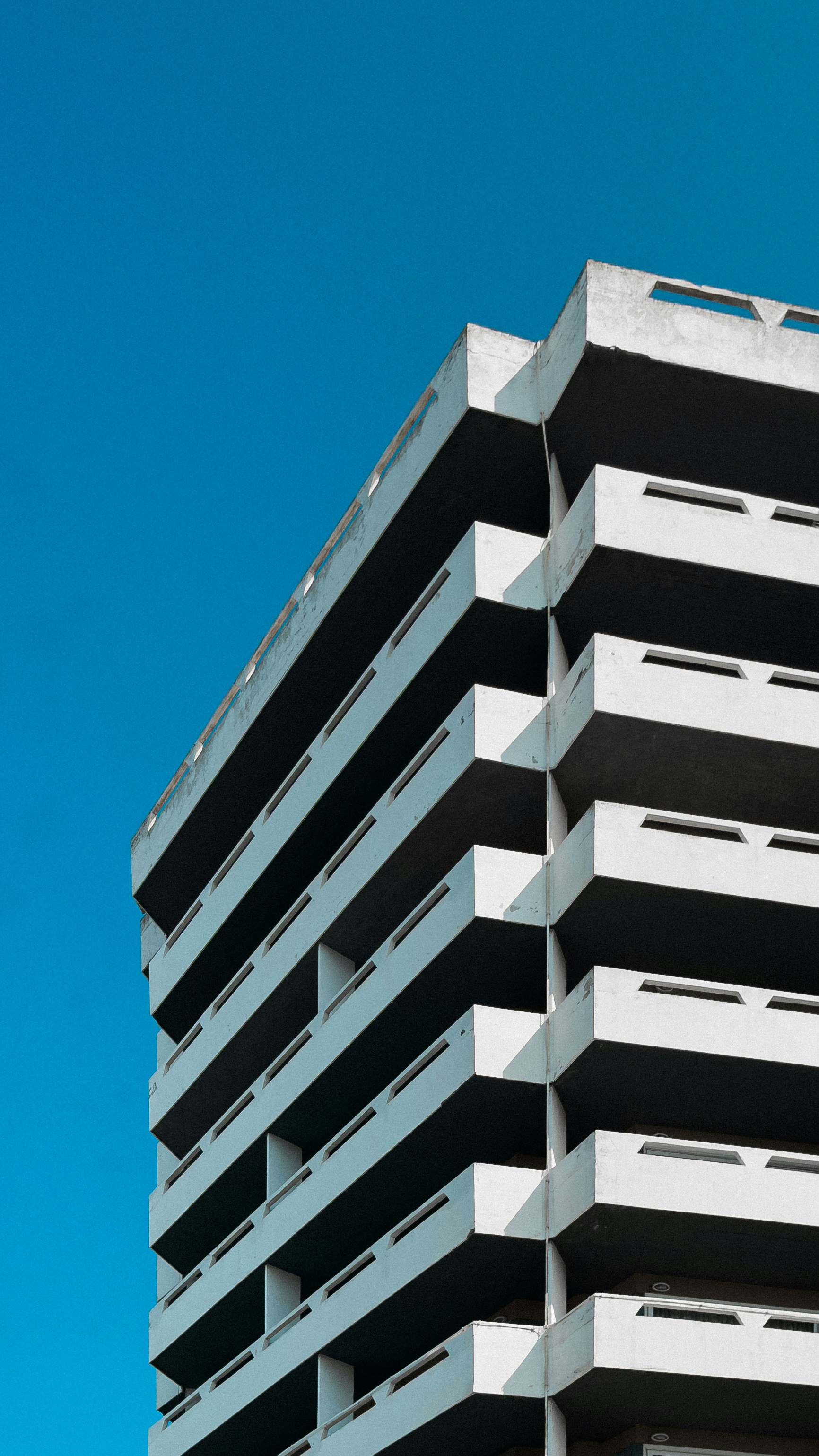 A corner view of a brutalist concrete apartment building against a clear blue sky