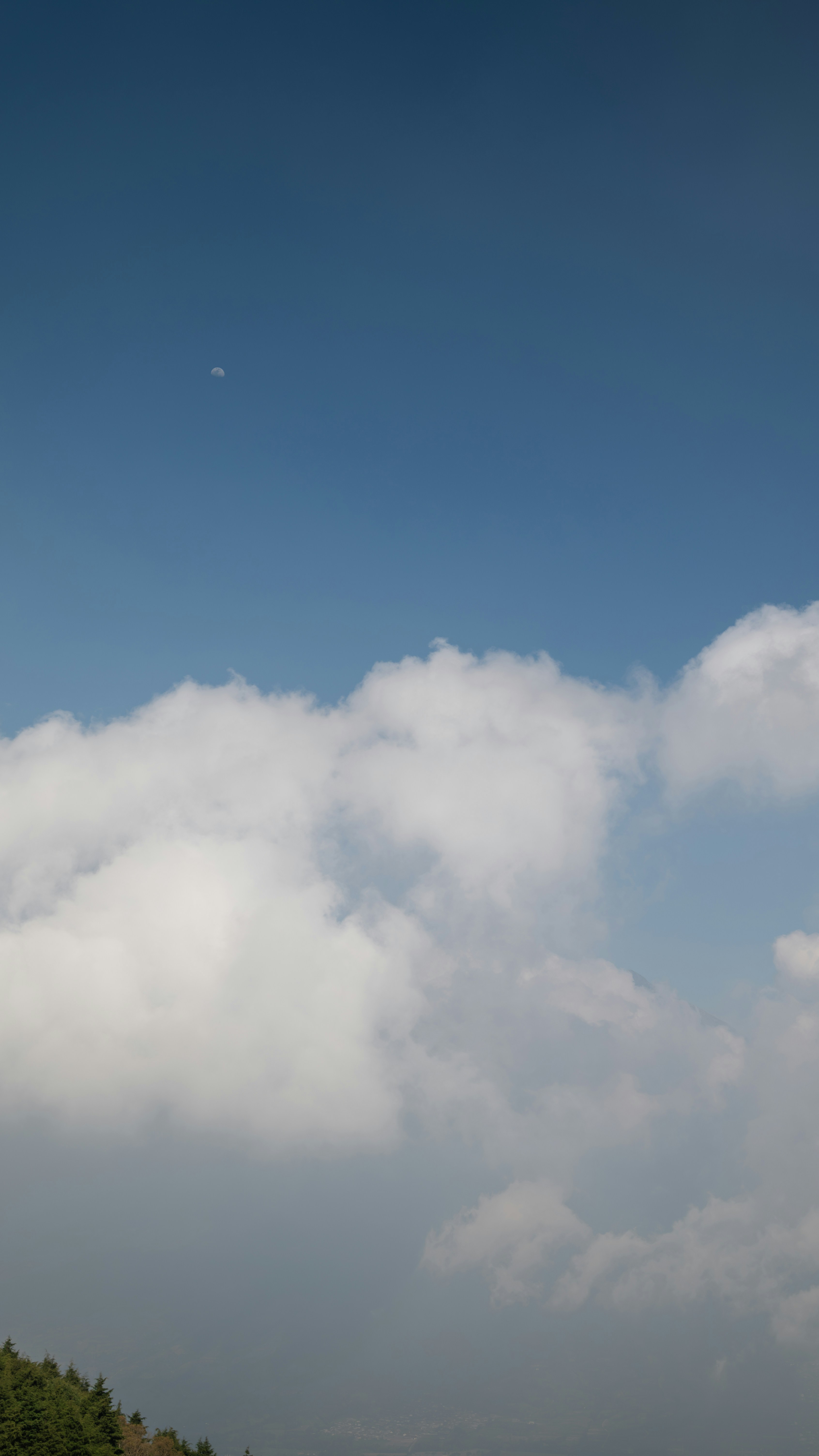 A small moon in a clear blue sky above white cumulus clouds