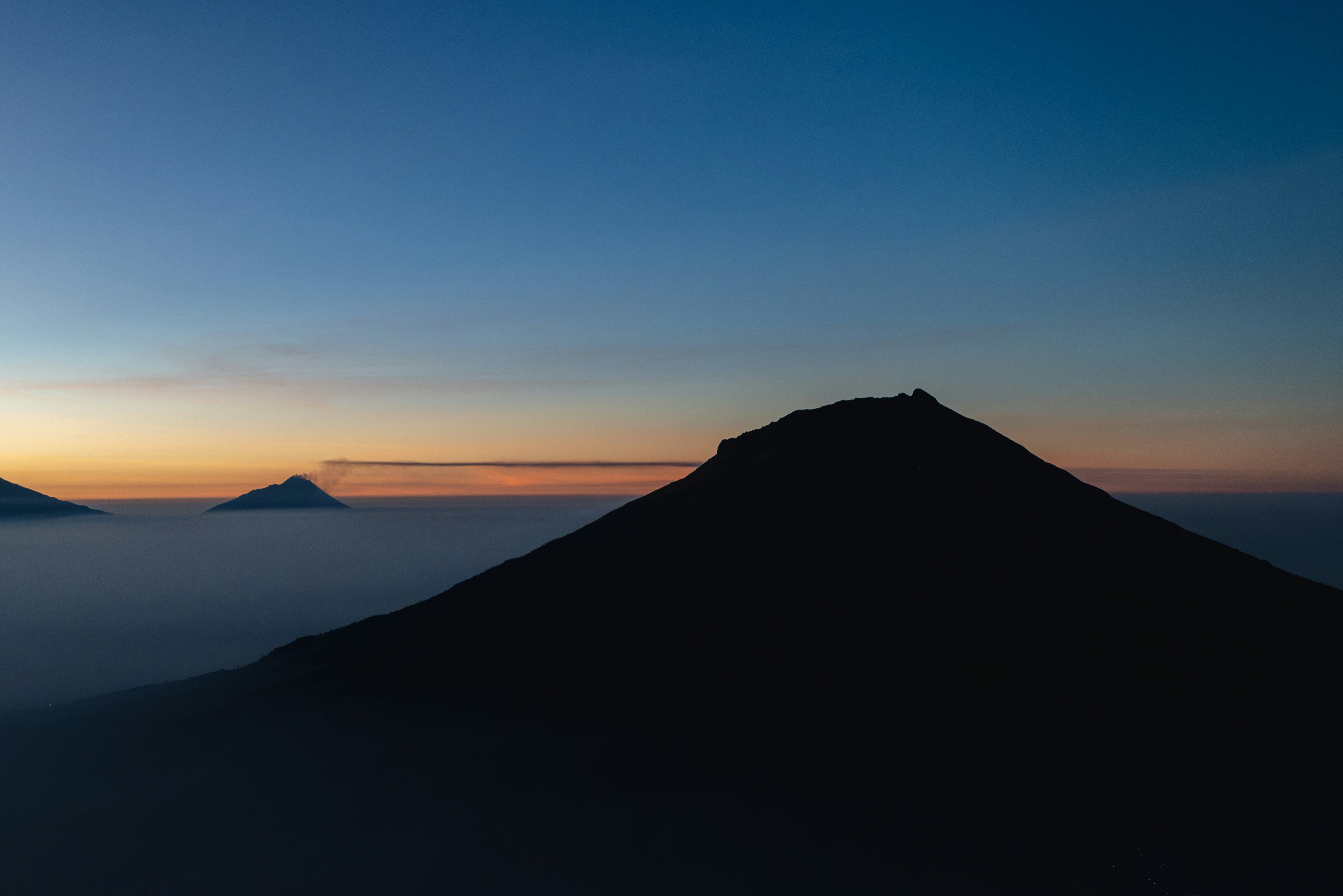 Silhouettes of volcanic peaks rising above a thick layer of low clouds